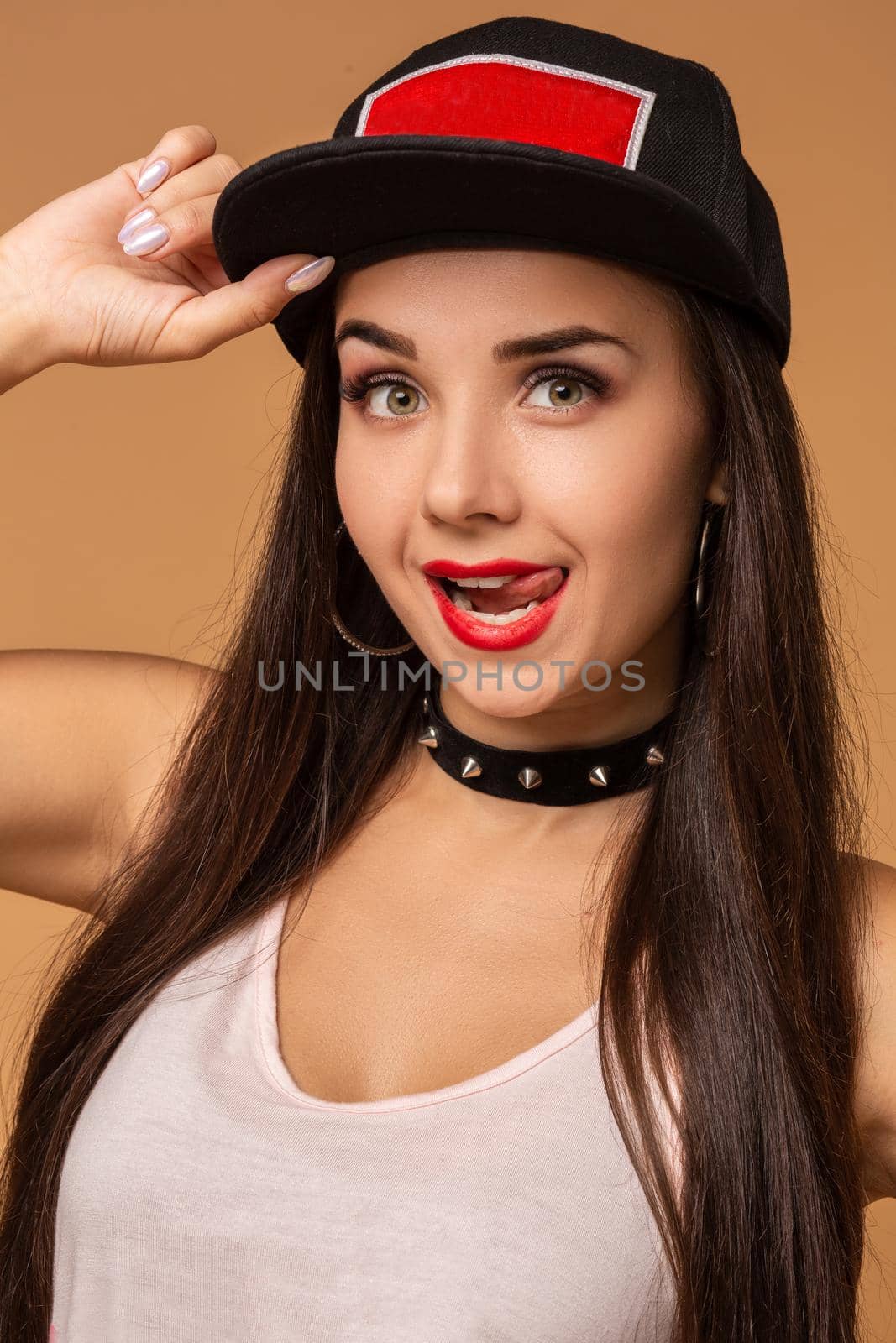 Hip-hop girl in cap with long dark hair. Fashion portrait of modern young woman in cap on beige background.