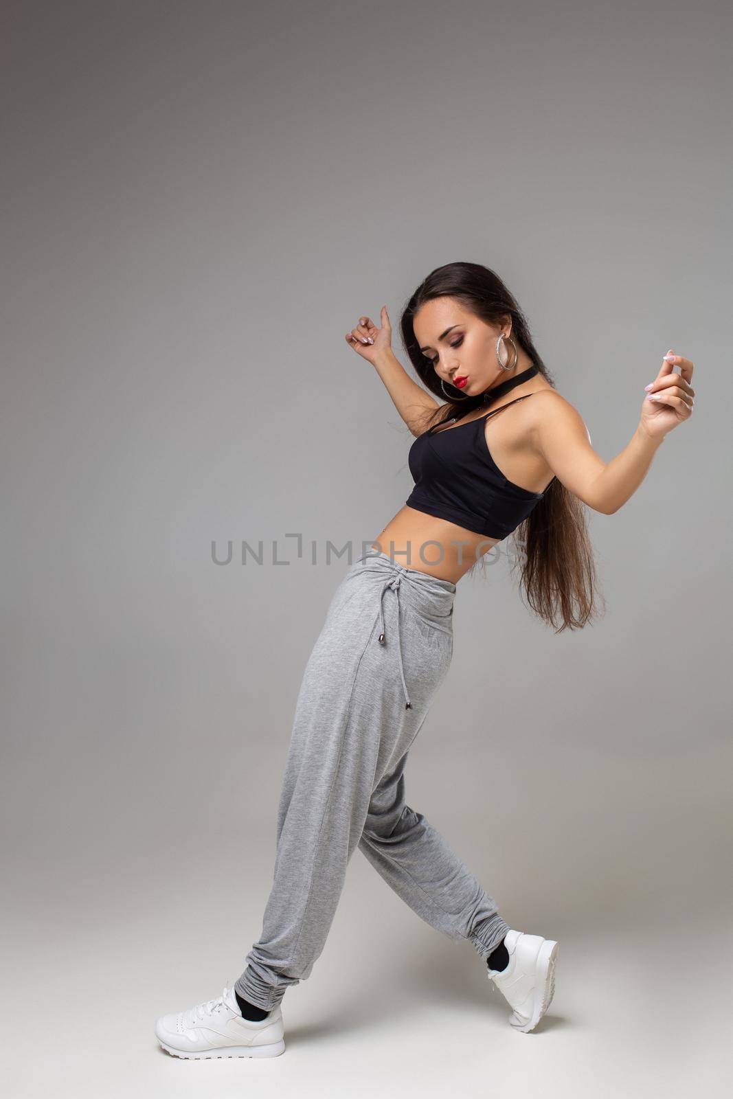 Modern dancer poses in front of the gray studio background. Modern dance styles, dancehall, jazz funk, hip hop