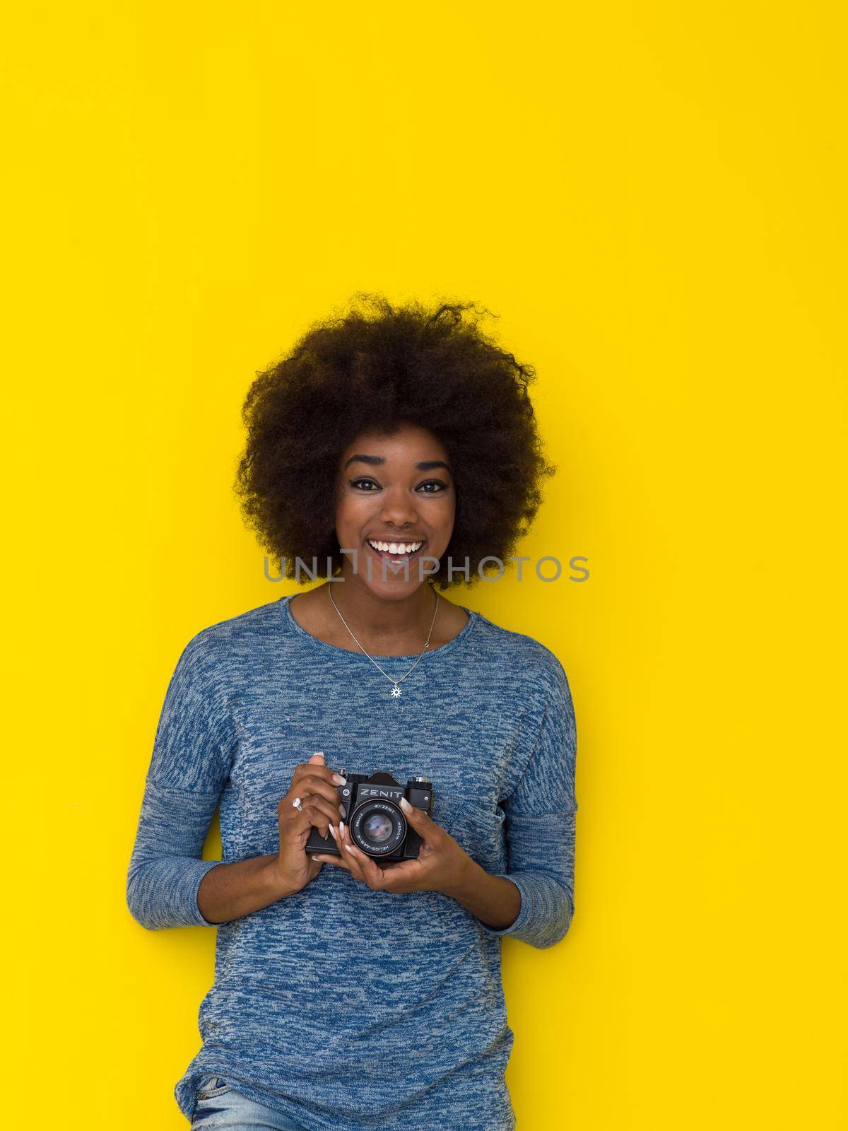 portrait of a smiling pretty african american girl taking photo on a retro camera isolated over yellow background