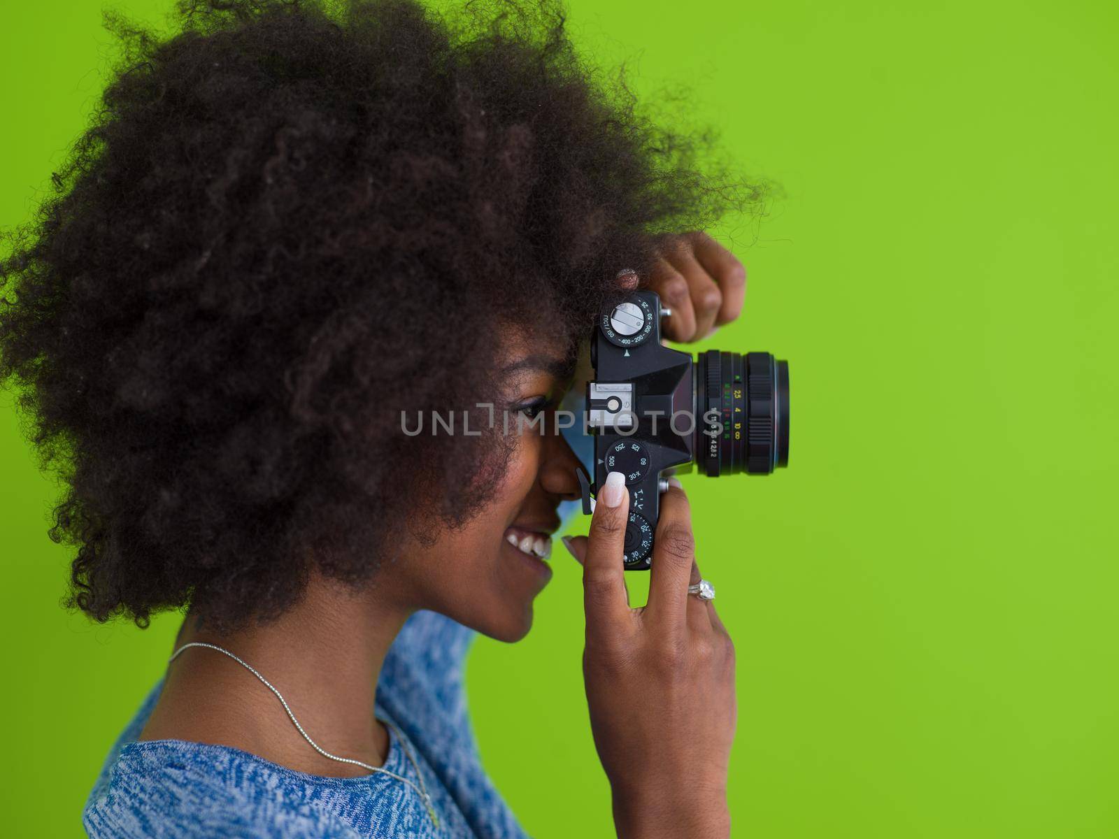 portrait of a smiling pretty african american girl taking photo on a retro camera isolated over green background
