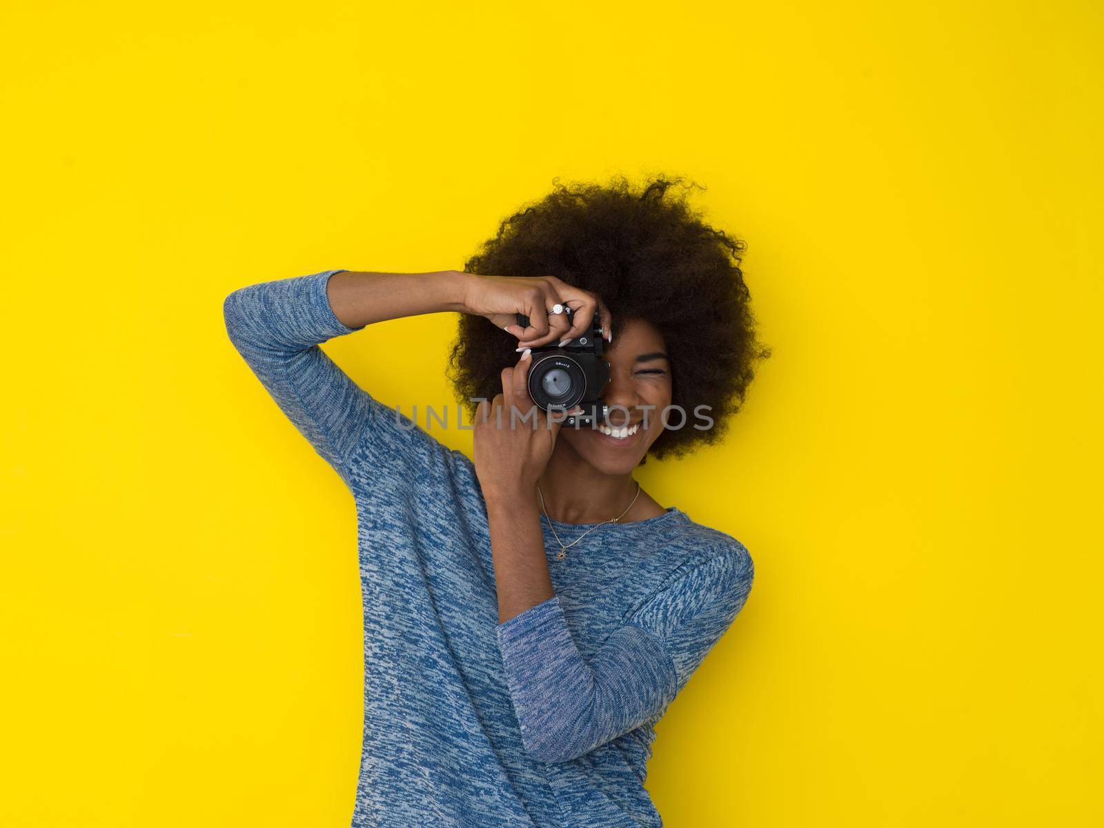 portrait of a smiling pretty african american girl taking photo on a retro camera isolated over yellow background