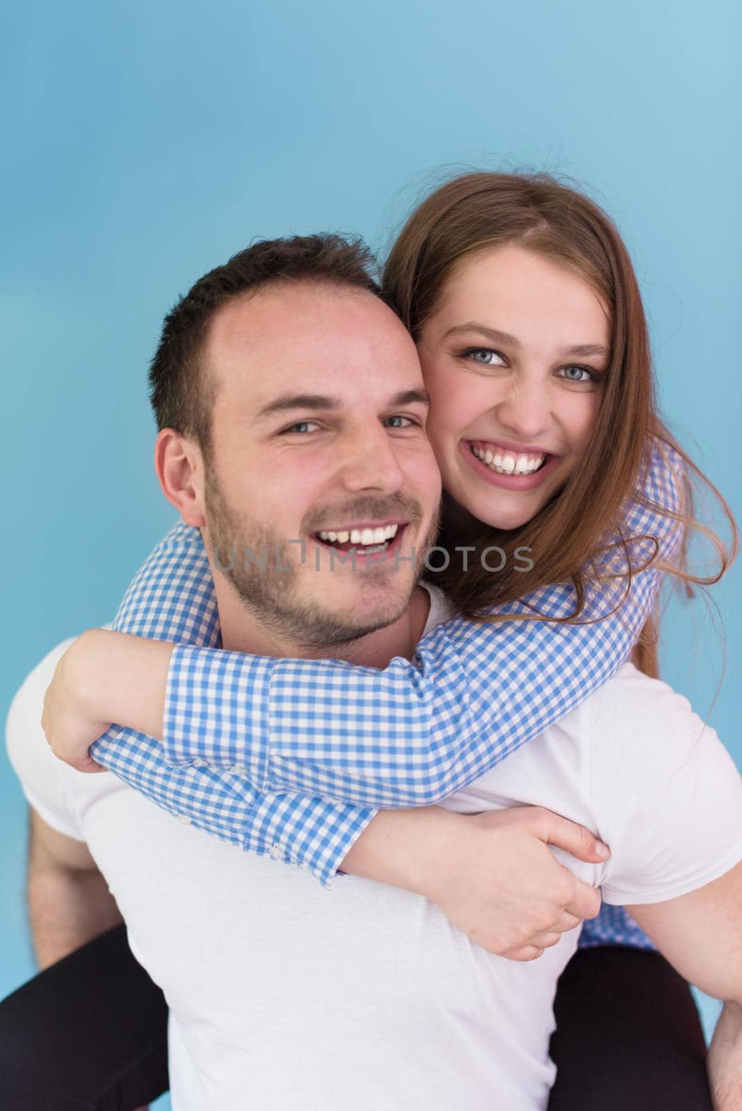 happy young man piggybacking his girlfriend isolated on blue background