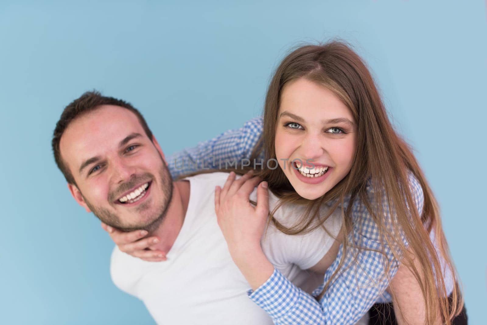 happy young man piggybacking his girlfriend isolated on blue background