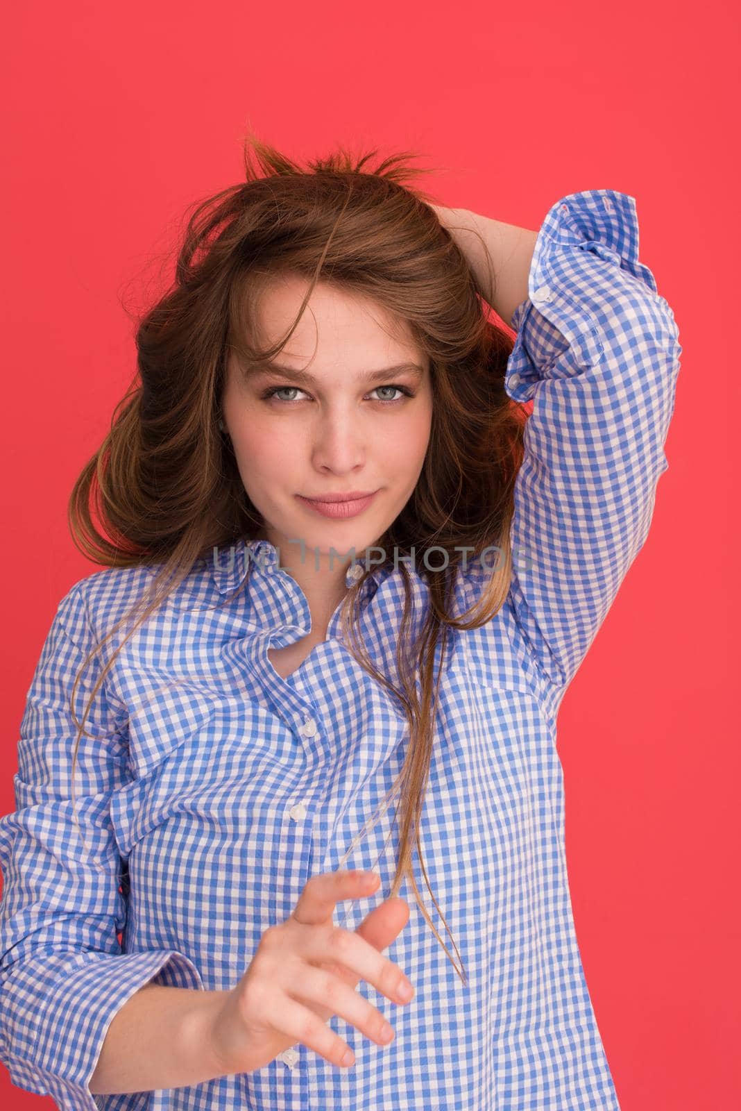 Portrait of a beautiful positive young woman while playing with her long silky hair isolated on red background