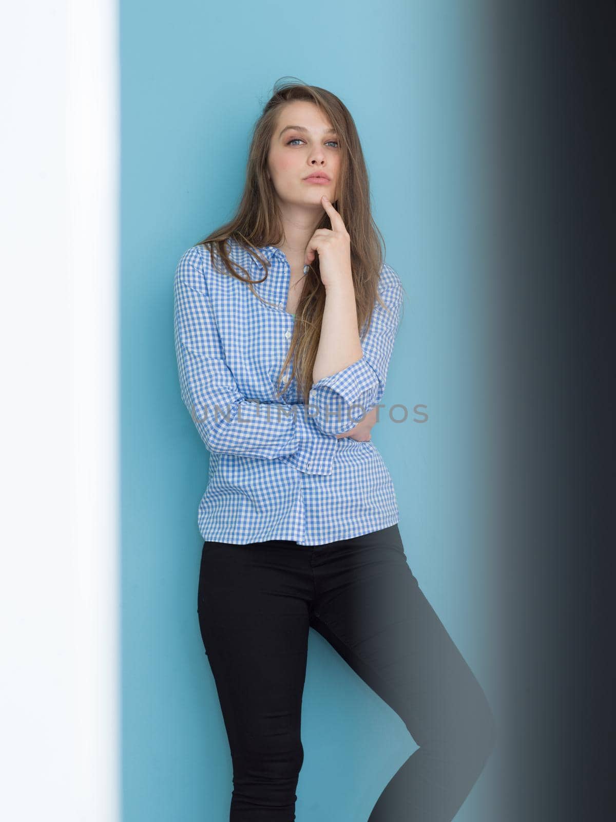 Portrait of a beautiful positive young woman while playing with her long silky hair isolated on blue background