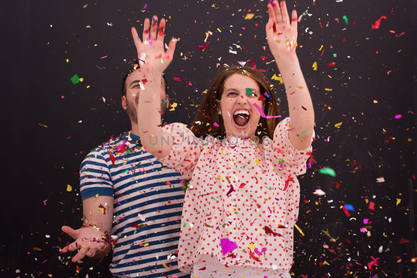 handsome young couple celebrating new year and chrismas party while blowing confetti decorations to camera isolated over gray background
