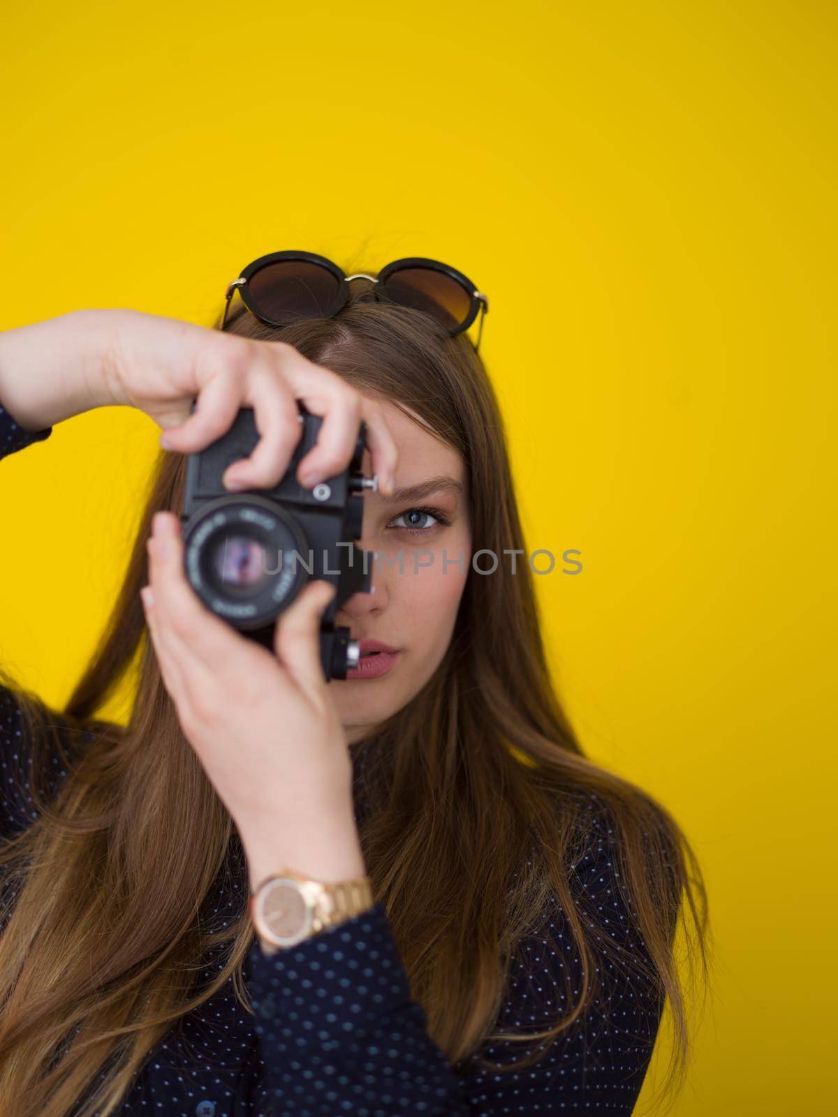 portrait of a smiling pretty girl taking photo on a retro camera isolated over yellow background