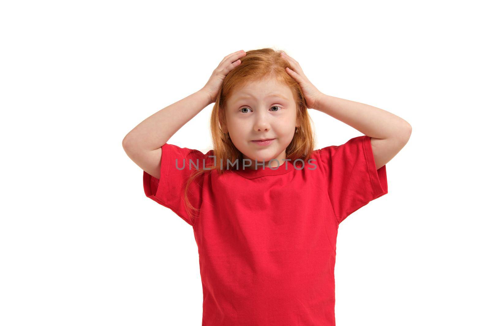 Portrait of cute redhead emotional little girl in red t-shirt isolated on a white. Beautiful studio portrait of female little caucasian person holding her head stressed