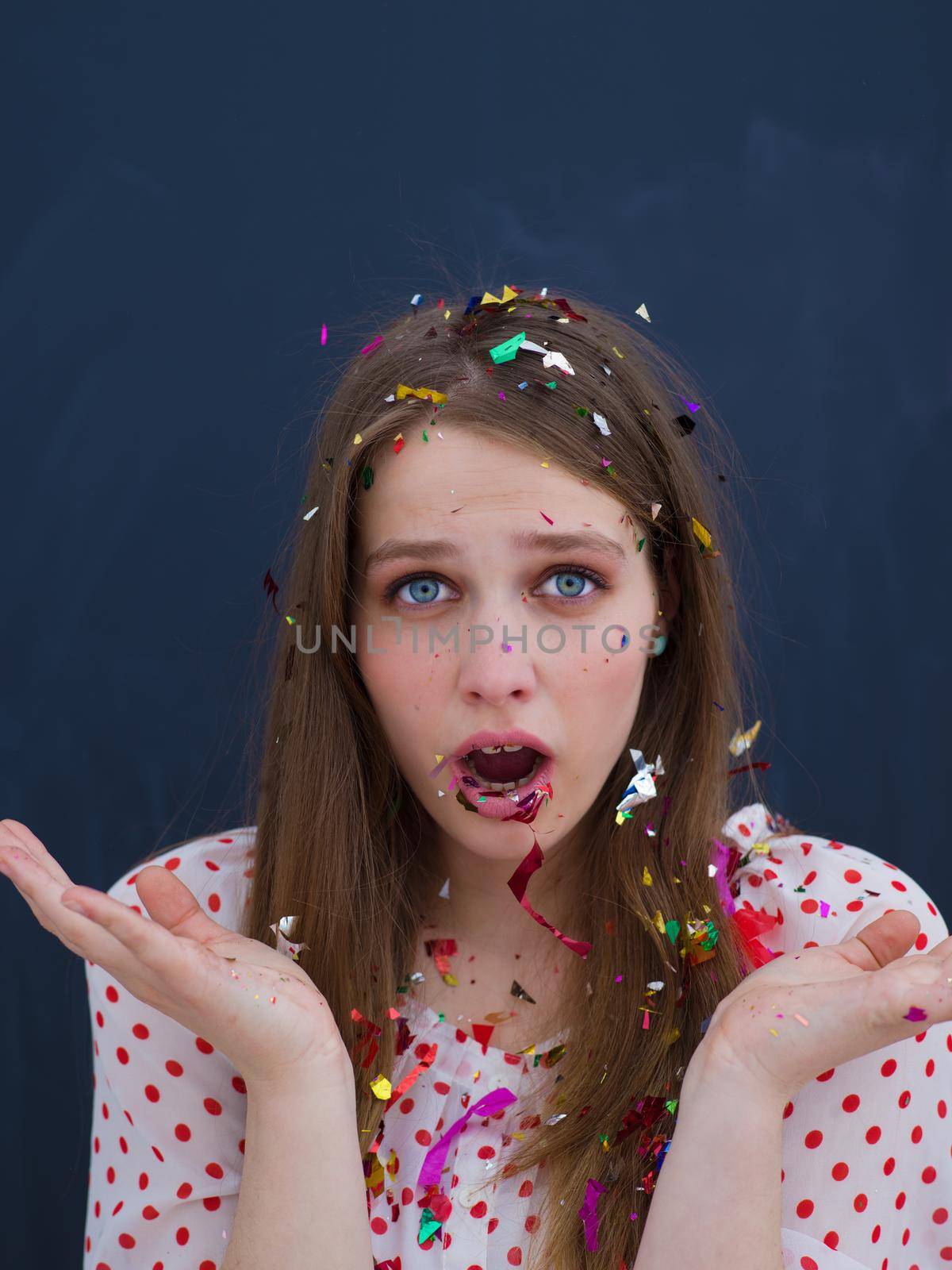 beautiful young woman celebrating new year and chrismas party while blowing confetti decorations to camera isolated over gray background