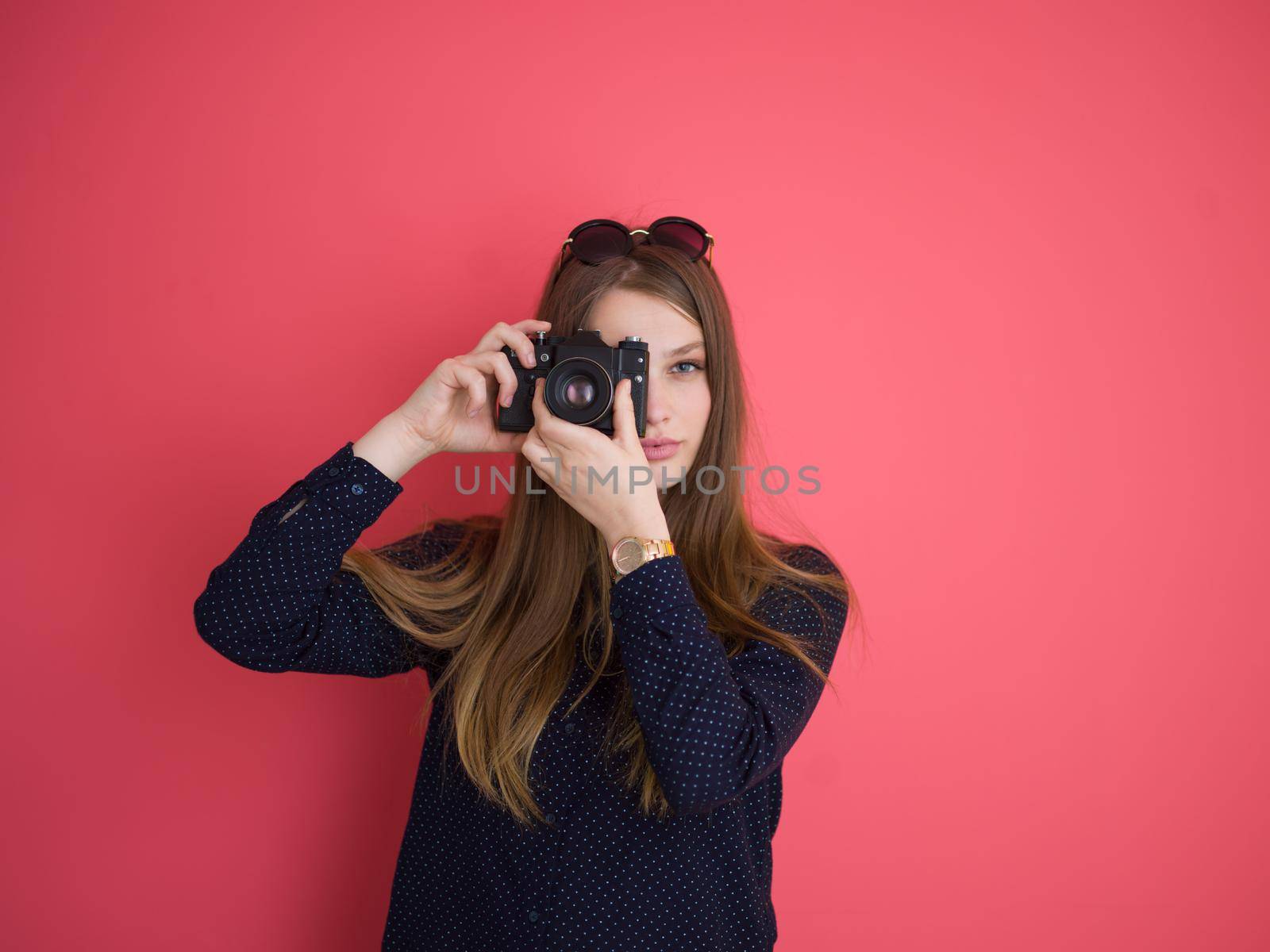 portrait of a smiling pretty girl taking photo on a retro camera isolated over red background