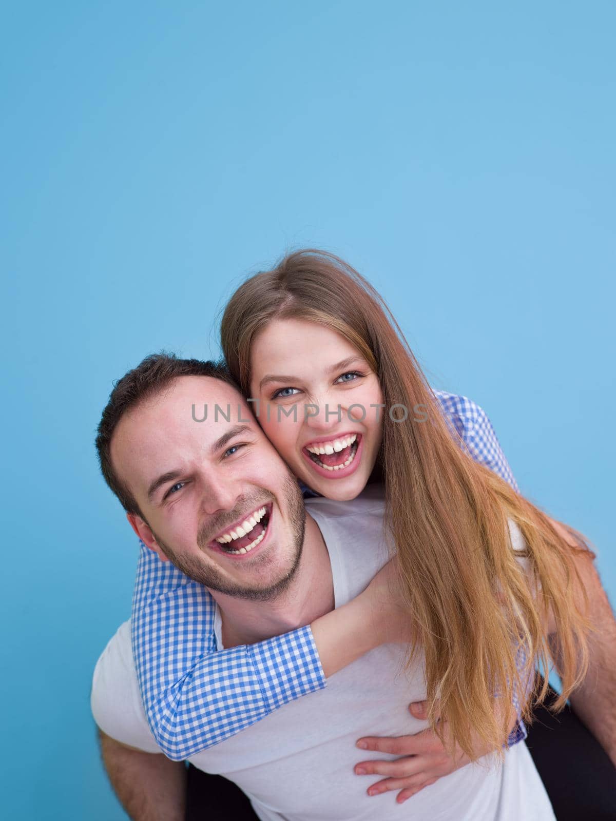 happy young man piggybacking his girlfriend isolated on blue background