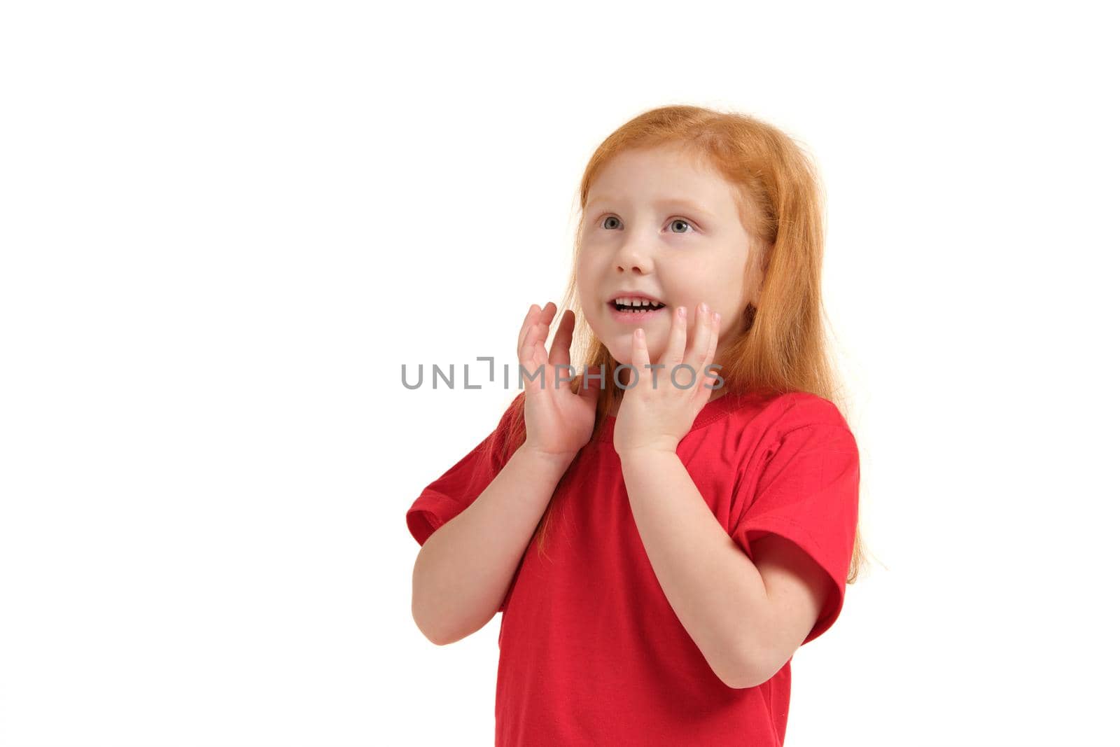 What a surprise. Pleasant cute upbeat little girl holding her hands near face and smiling while expressing joy.