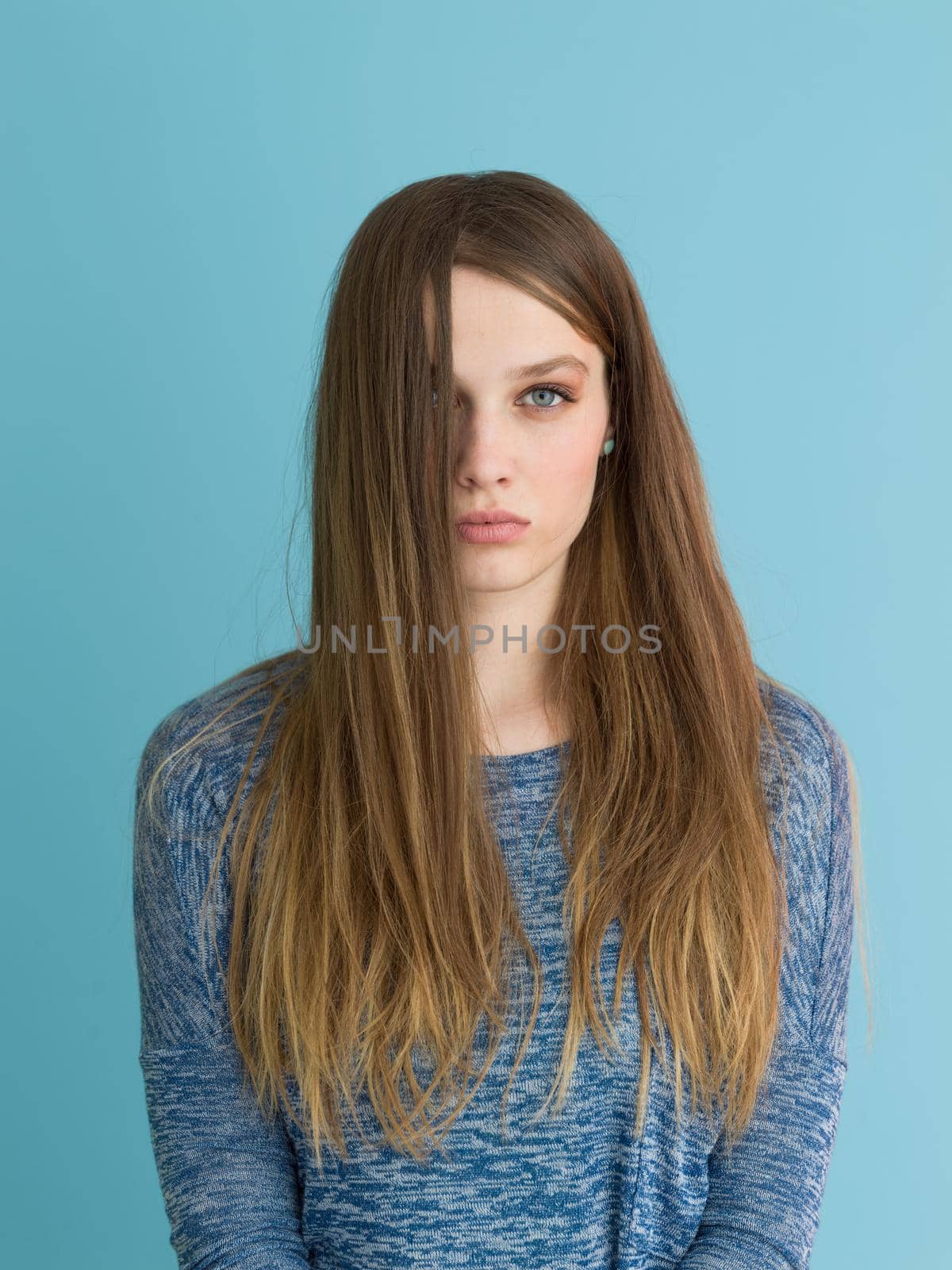 Portrait of a beautiful positive young woman while playing with her long silky hair isolated on blue background