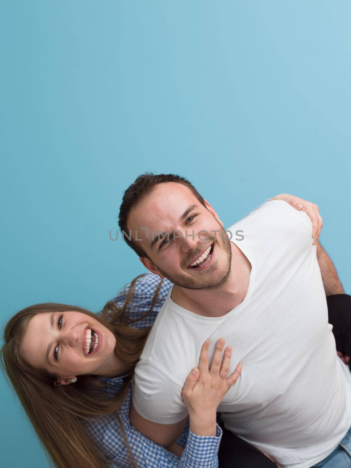 happy young man piggybacking his girlfriend isolated on blue background