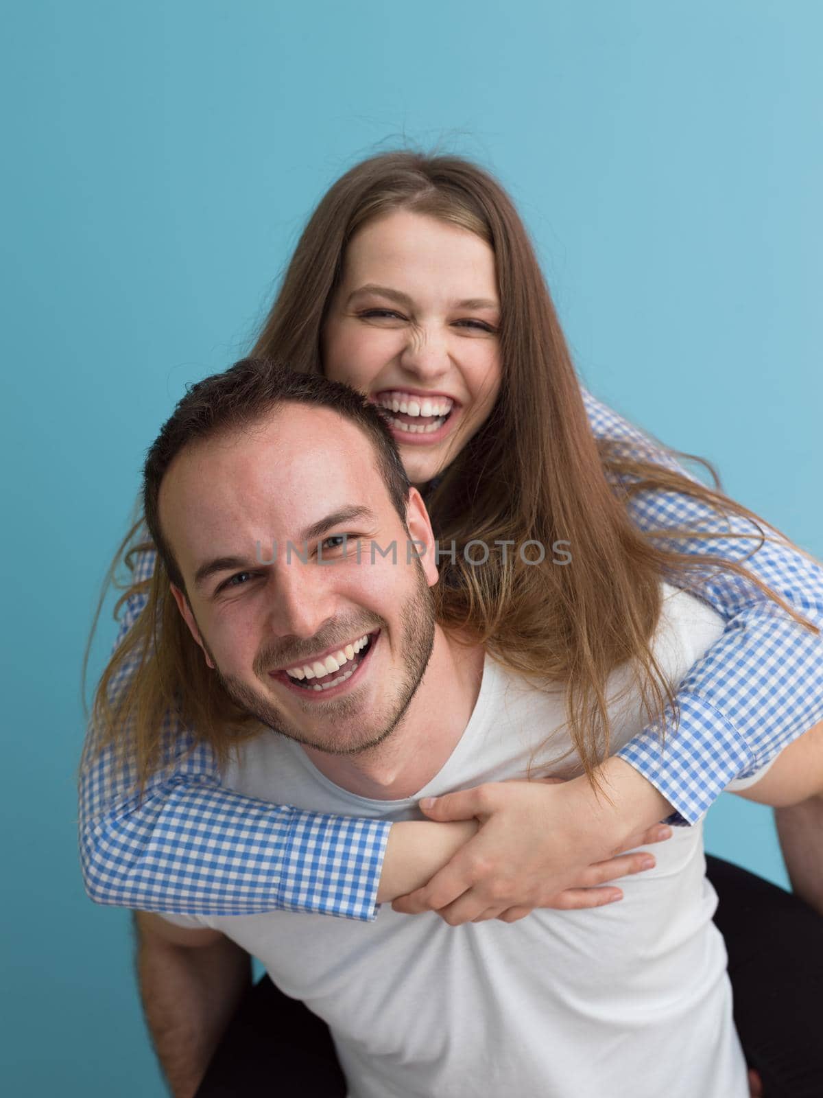 happy young man piggybacking his girlfriend isolated on blue background