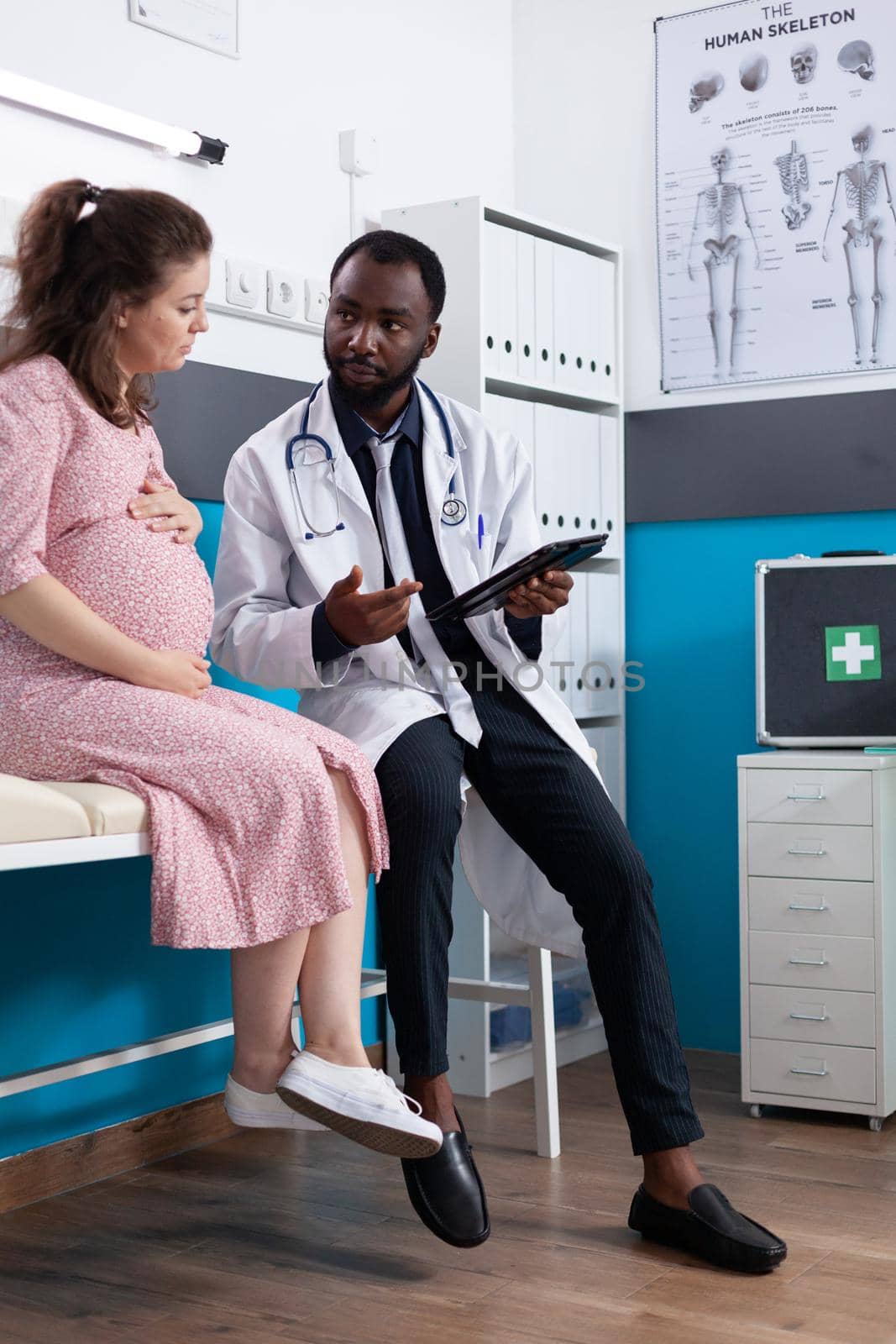Medic showing digital device with diagnosis to pregnant patient by DCStudio