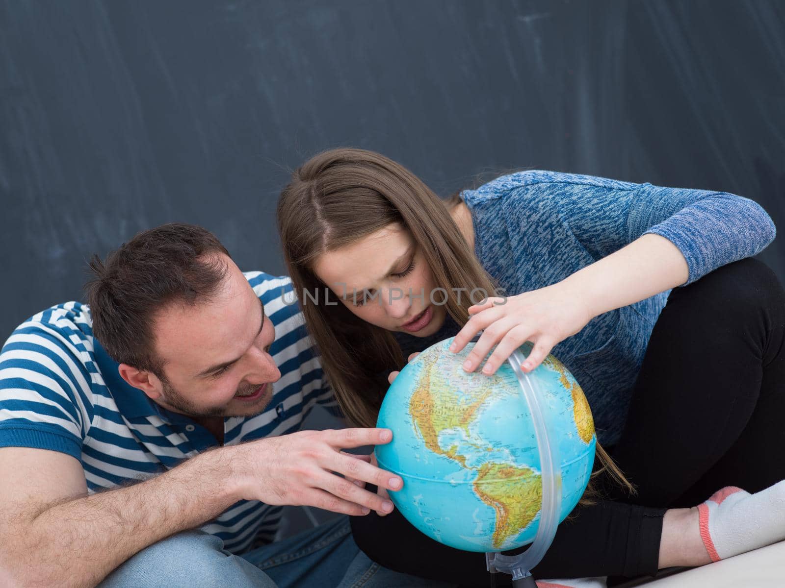 Young lovely couple in casual clothing investigating globe isolated over gray background