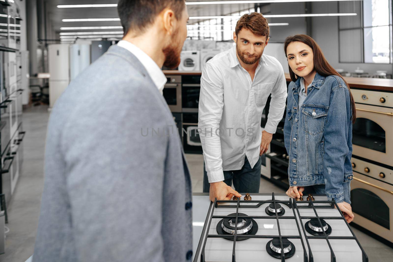 Male shop assistant helps young couple to choose new home appliance in hypermarket