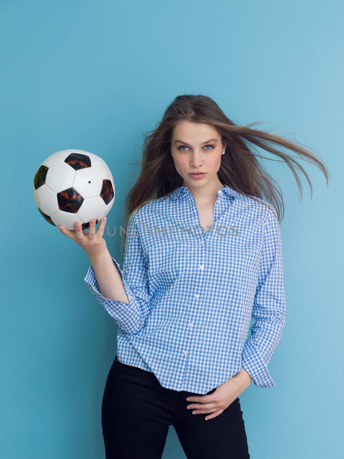 Portrait of a beautiful positive young woman while playing with a soccer ball isolated on blue background