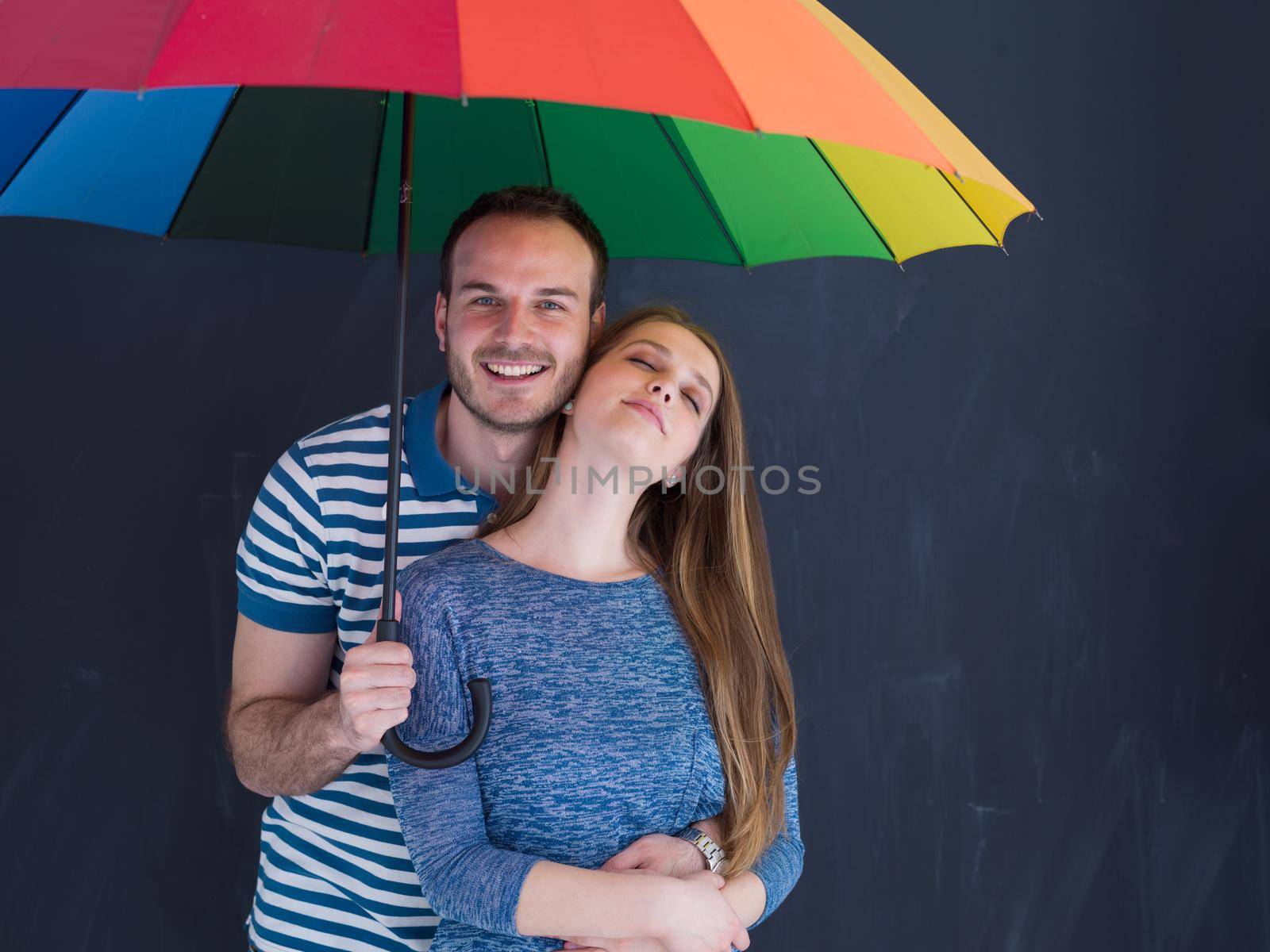 portrait of a beautiful loving young couple with a colorful umbrella isolated on a gray background