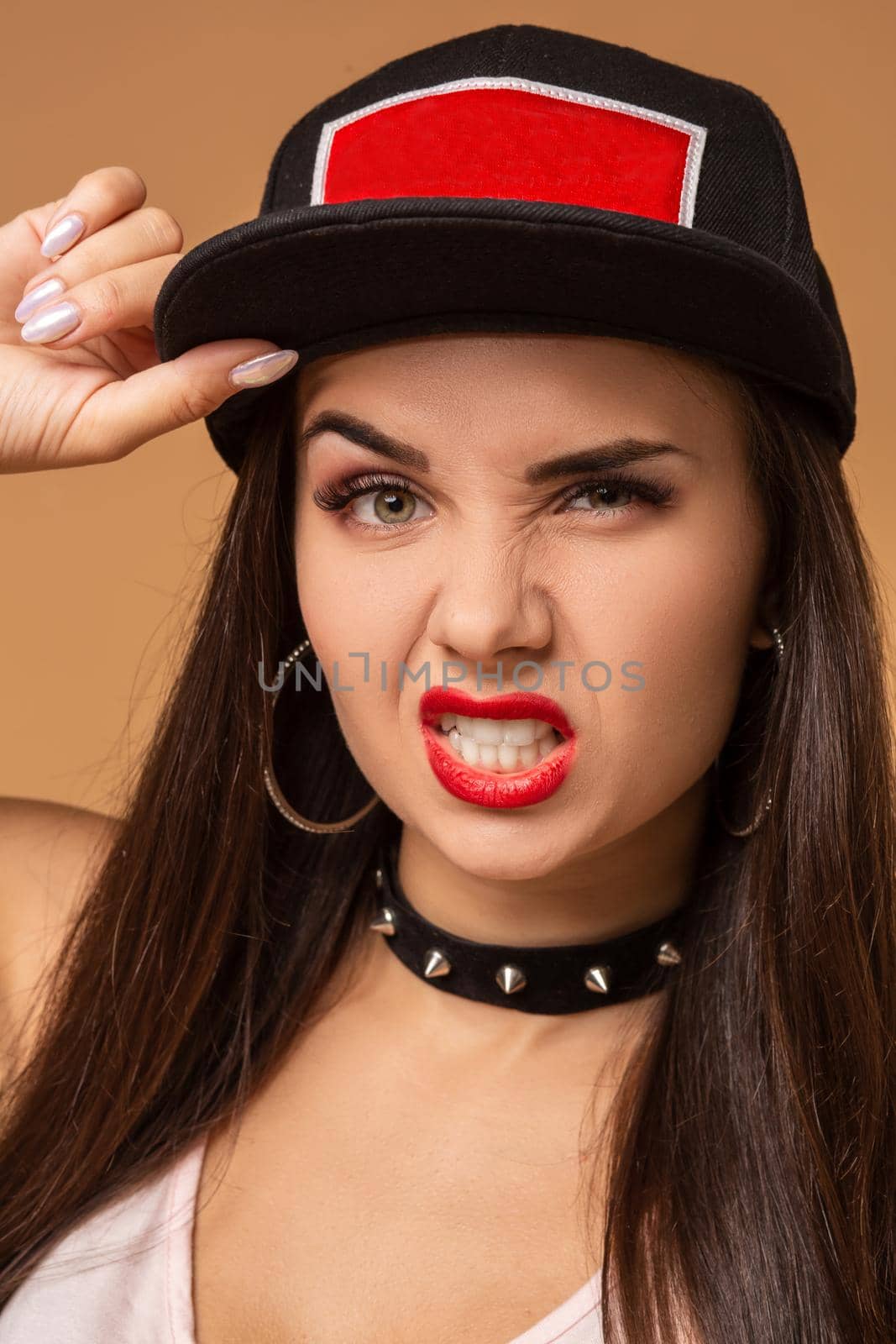 Hip-hop girl in cap with long dark hair. Fashion portrait of modern young woman in cap on beige background.