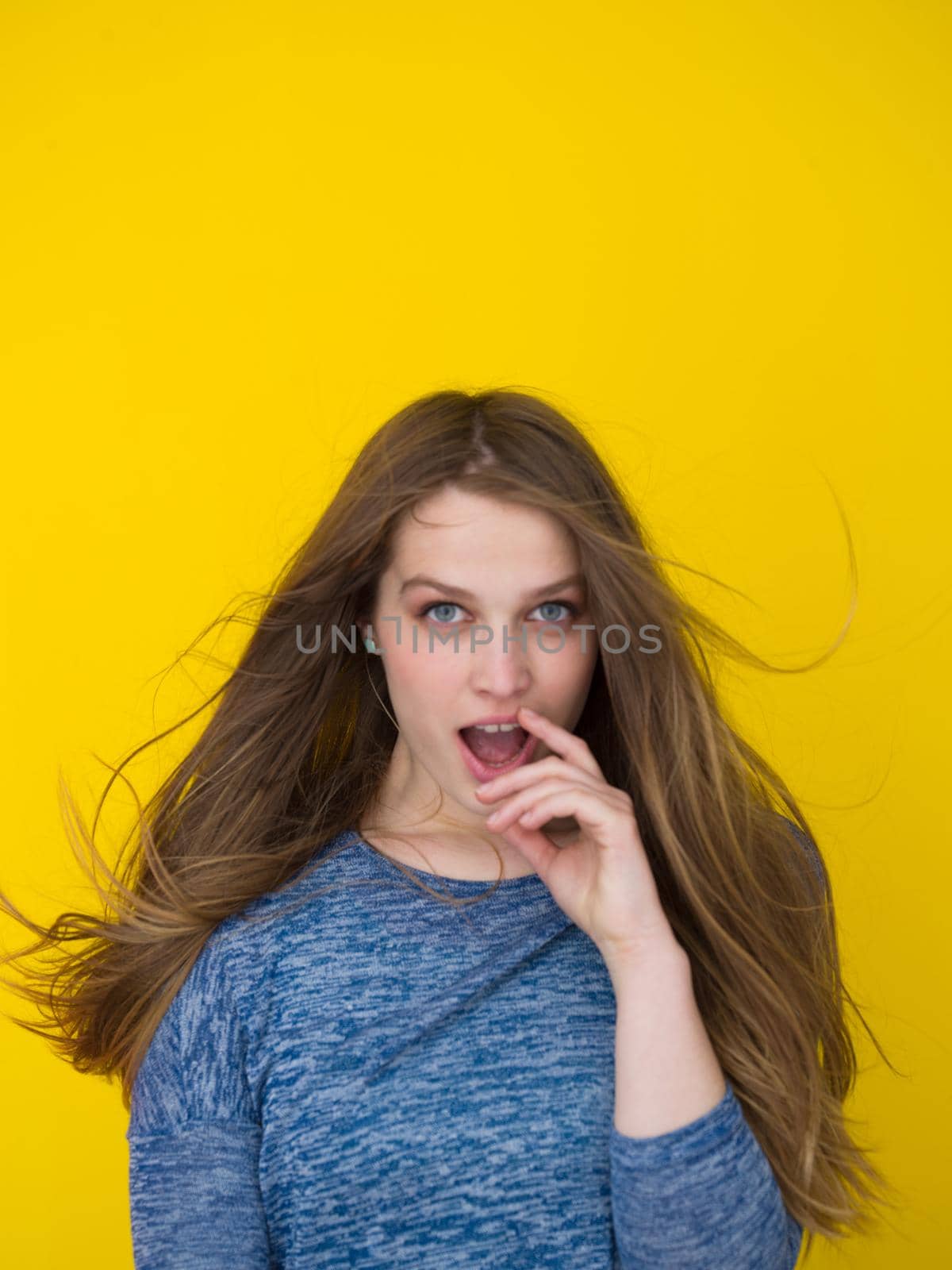 Portrait of a beautiful positive young woman while playing with her long silky hair isolated on yellow background