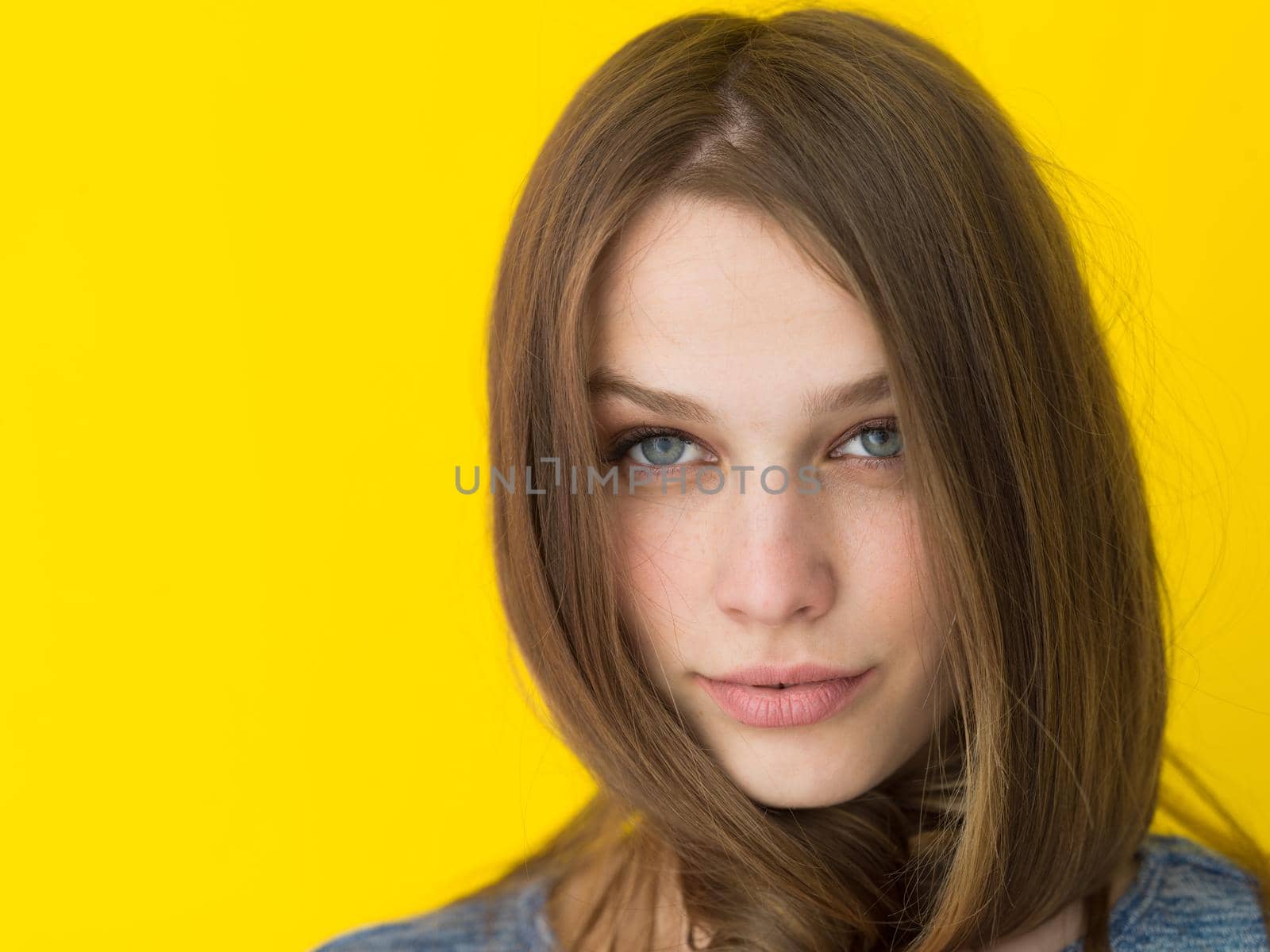Portrait of a beautiful positive young woman while playing with her long silky hair isolated on yellow background