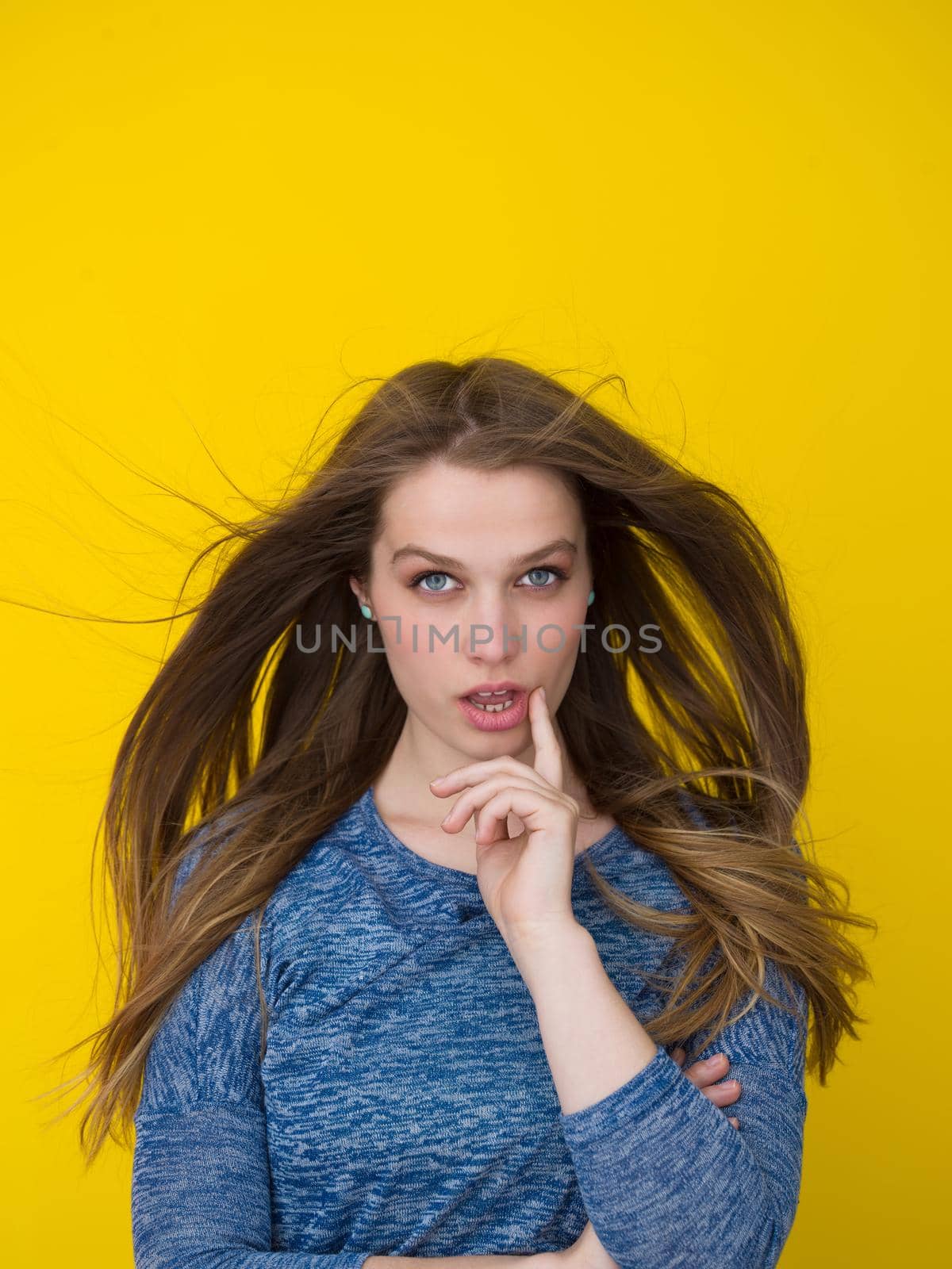 Portrait of a beautiful positive young woman while playing with her long silky hair isolated on yellow background