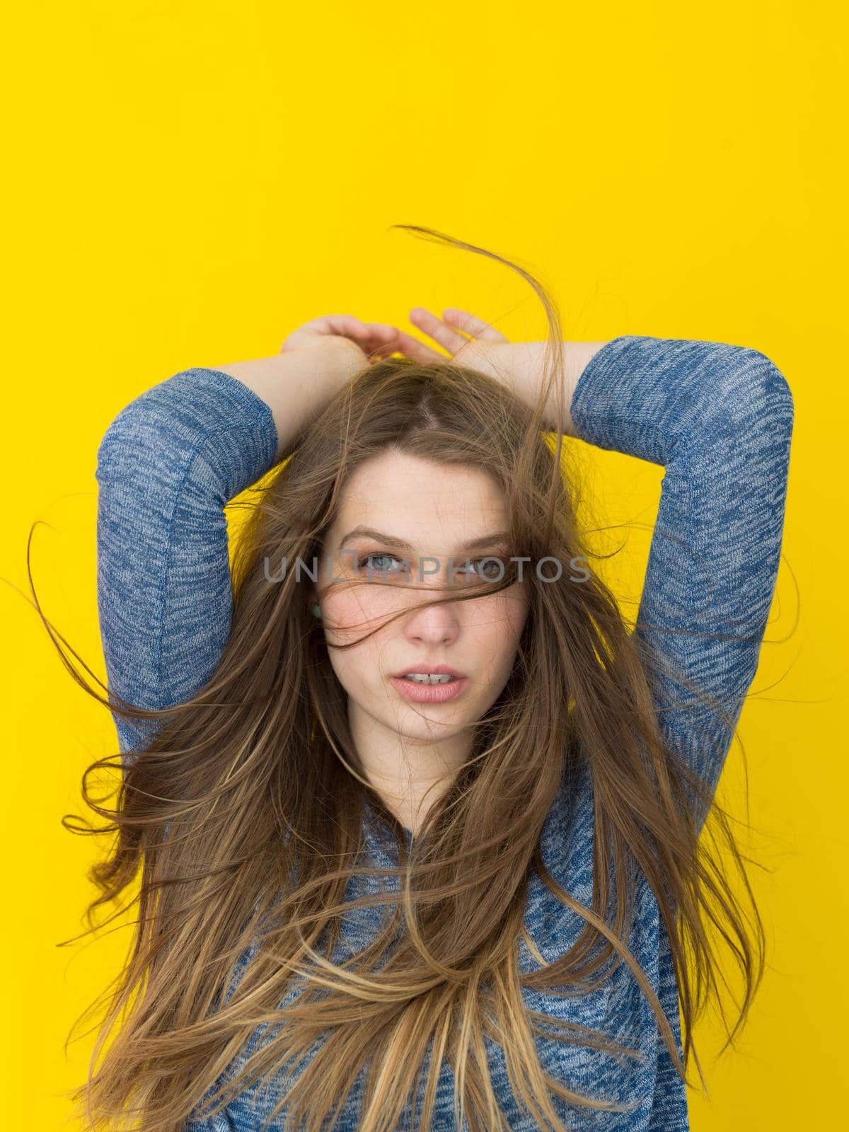 Portrait of a beautiful positive young woman while playing with her long silky hair isolated on yellow background