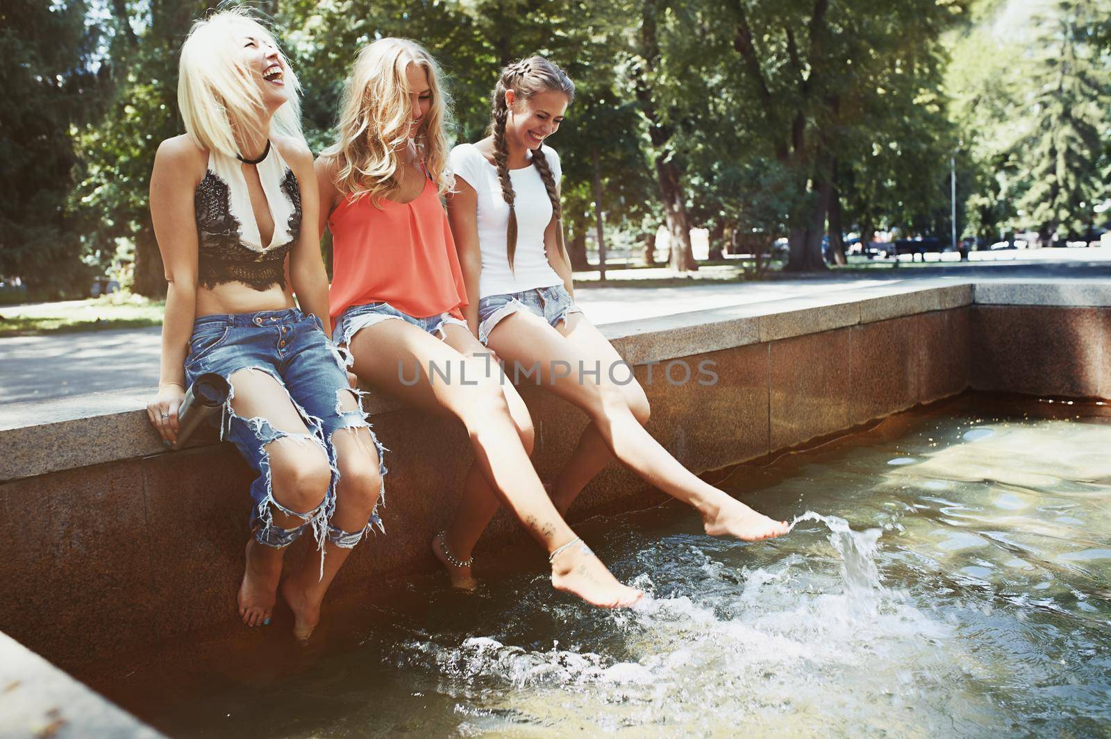 Girlfriends sitting at the fountain and dangling legs to the water