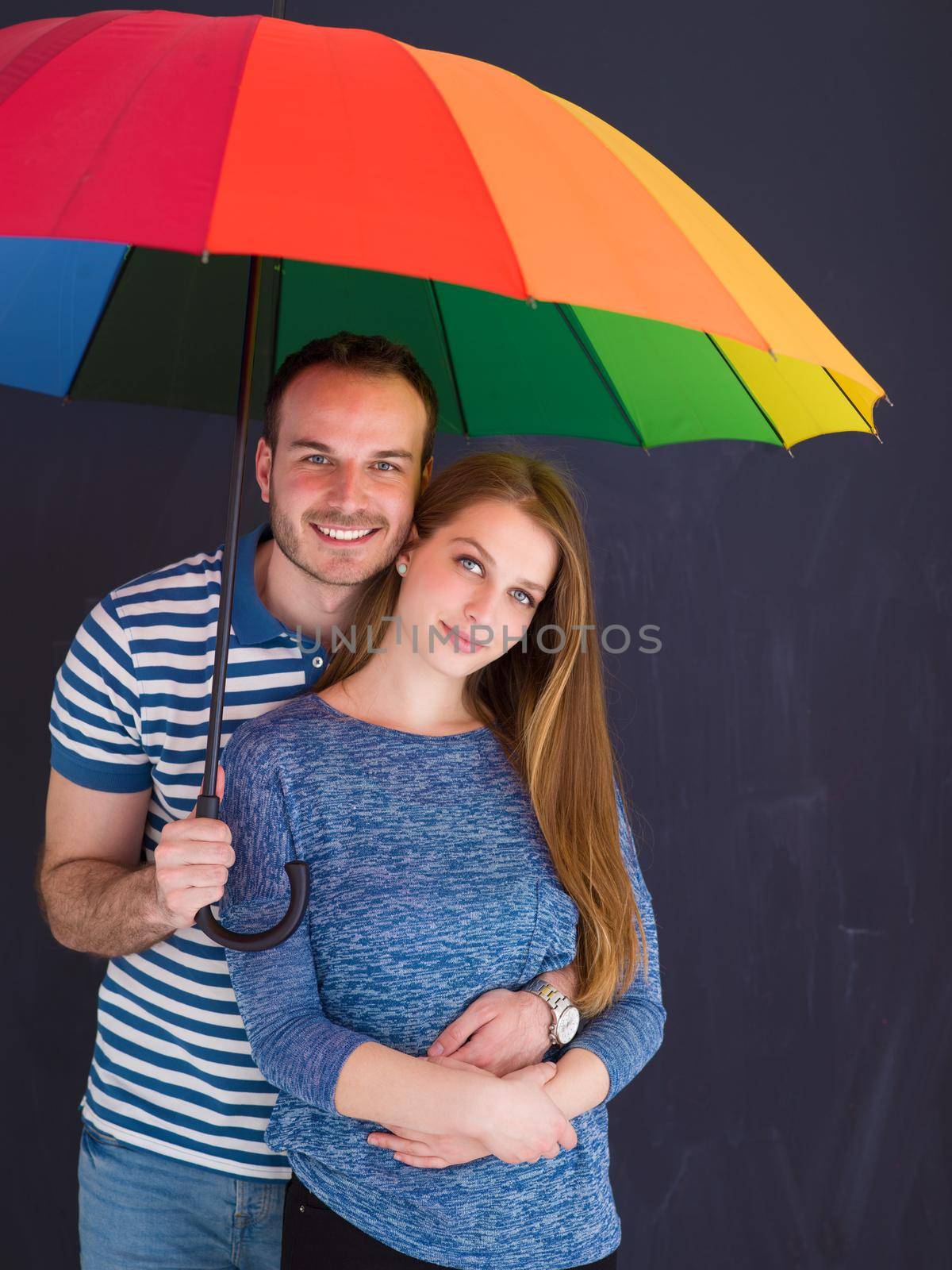 portrait of a beautiful loving young couple with a colorful umbrella isolated on a gray background