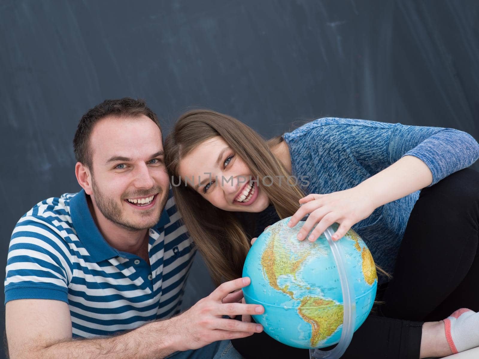 Young lovely couple in casual clothing investigating globe isolated over gray background