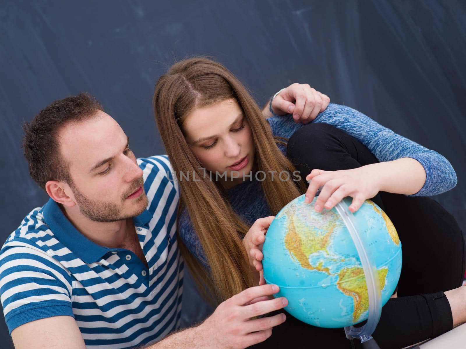 Young lovely couple in casual clothing investigating globe isolated over gray background