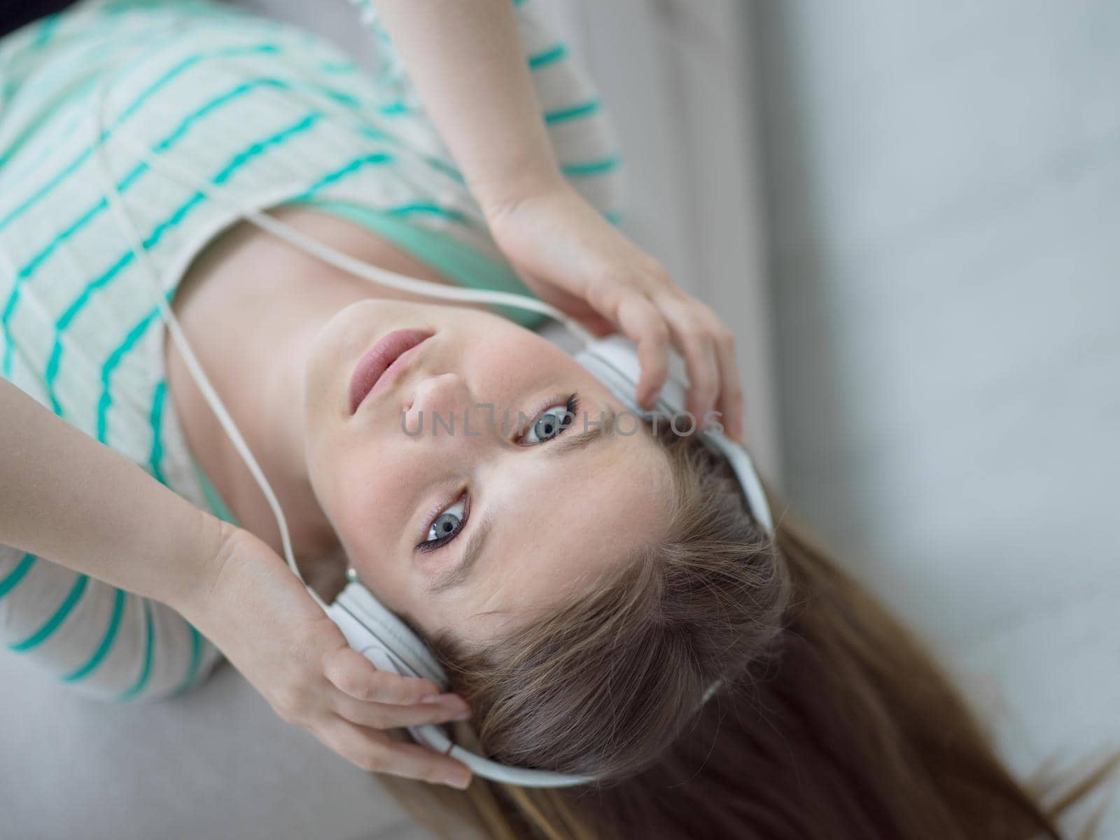 Young beautiful girl enjoying music through headphones, laying on sofa at home