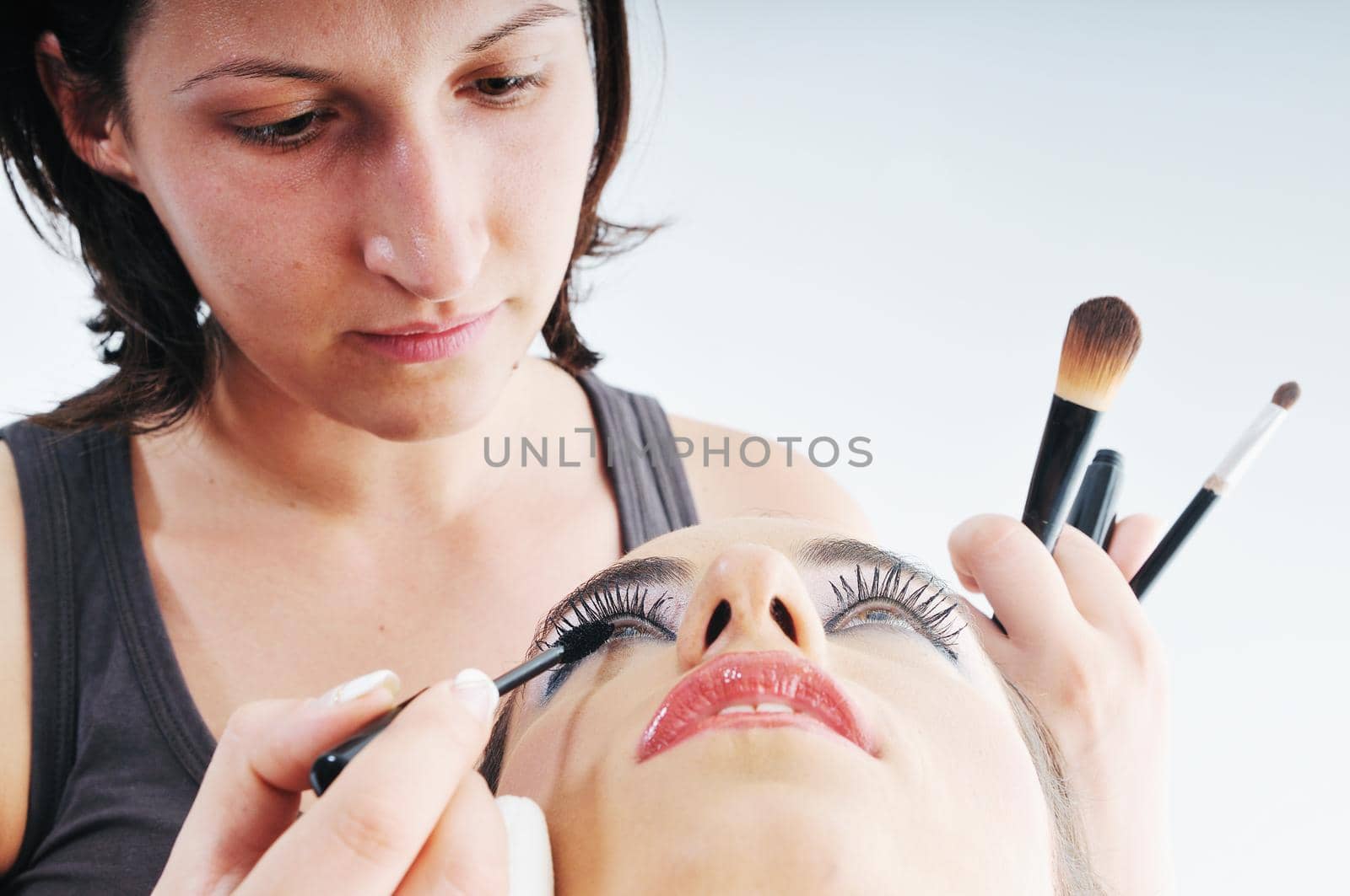 makeup treatment with professional makeup artist and beautiful brunette woman  isolated on white in studio