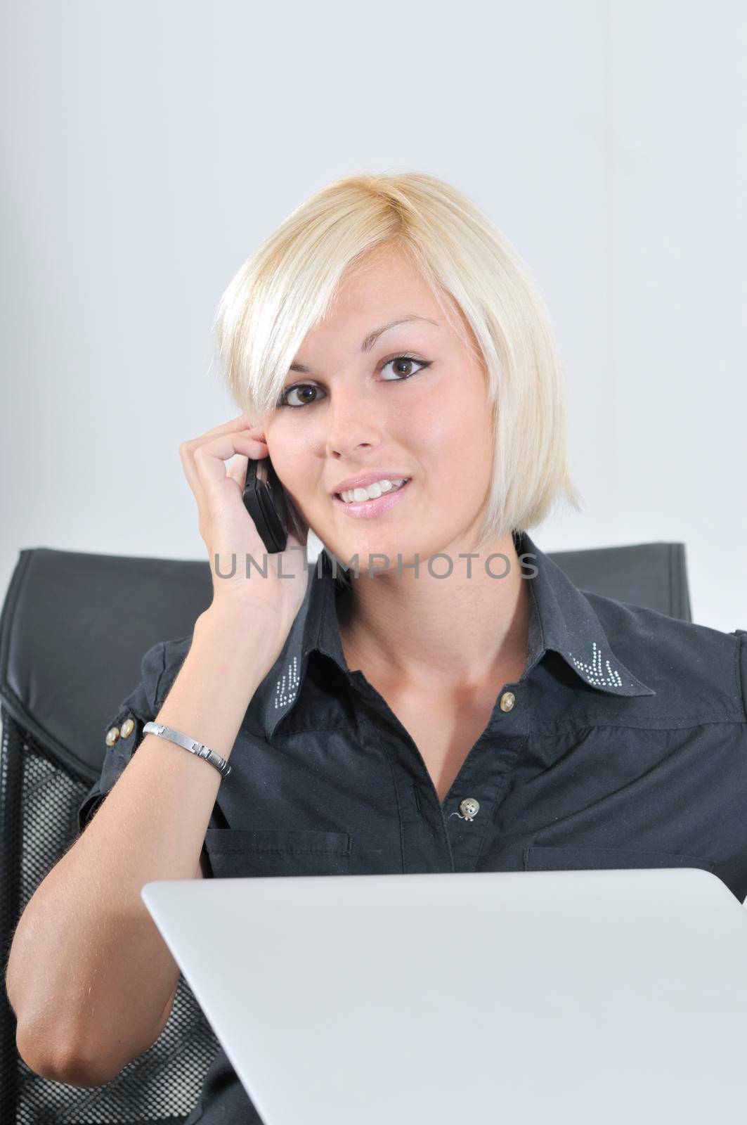 One young business blonde woman working in office on laptop and talking on cellphone, isolated image