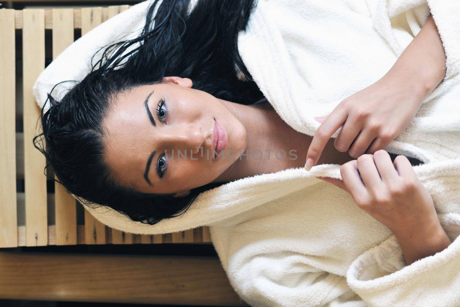 Pretty Young woman take a steam bath treatment at finish wooden sauna while wearing white towel