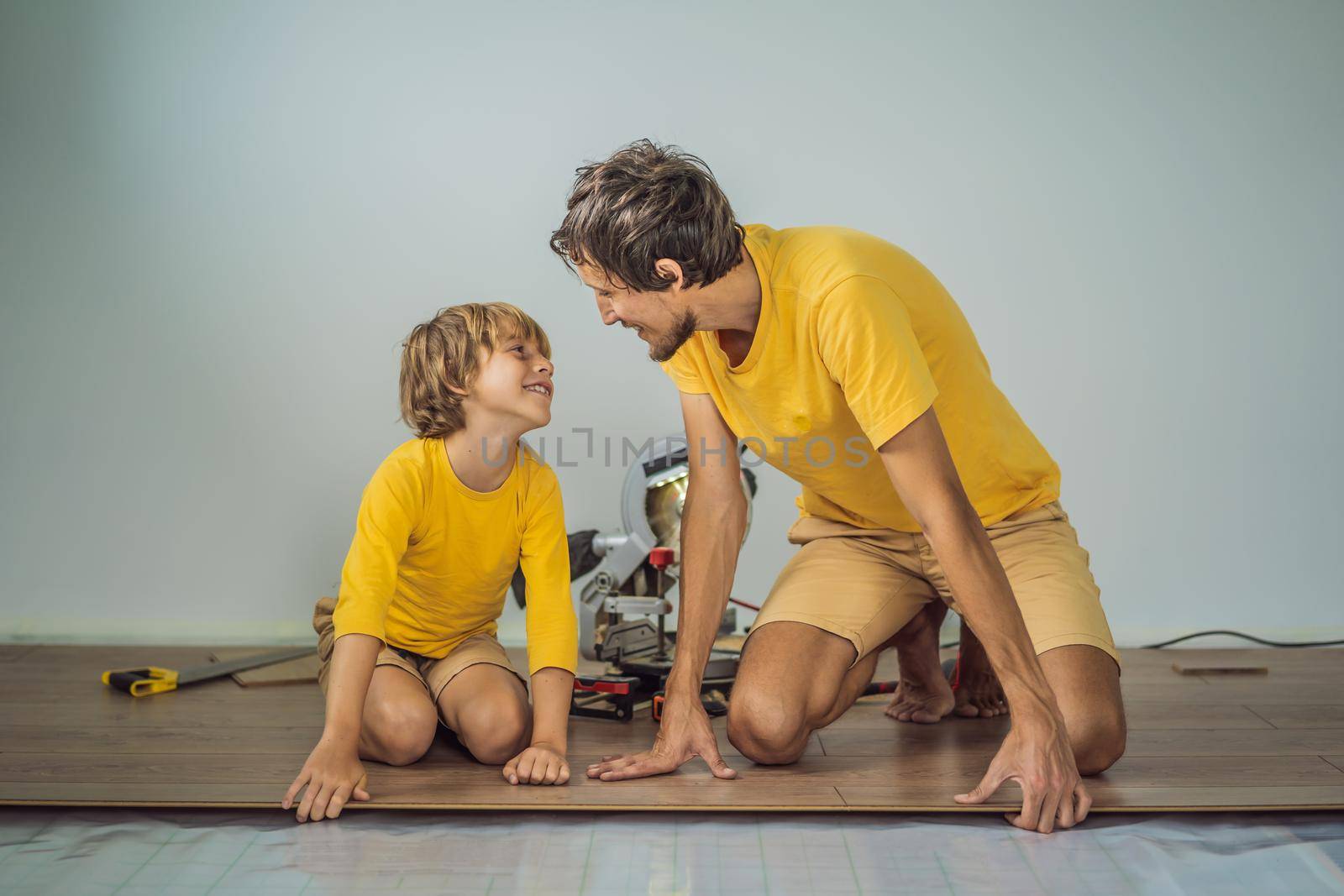 Father and son installing new wooden laminate flooring on a warm film floor. Infrared floor heating system under laminate floor.