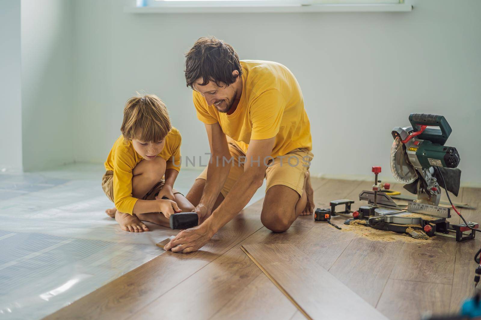 Father and son installing new wooden laminate flooring on a warm film floor. Infrared floor heating system under laminate floor by galitskaya