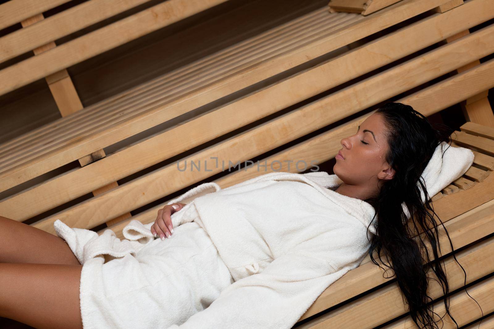 Pretty Young woman take a steam bath treatment at finish wooden sauna while wearing white towel