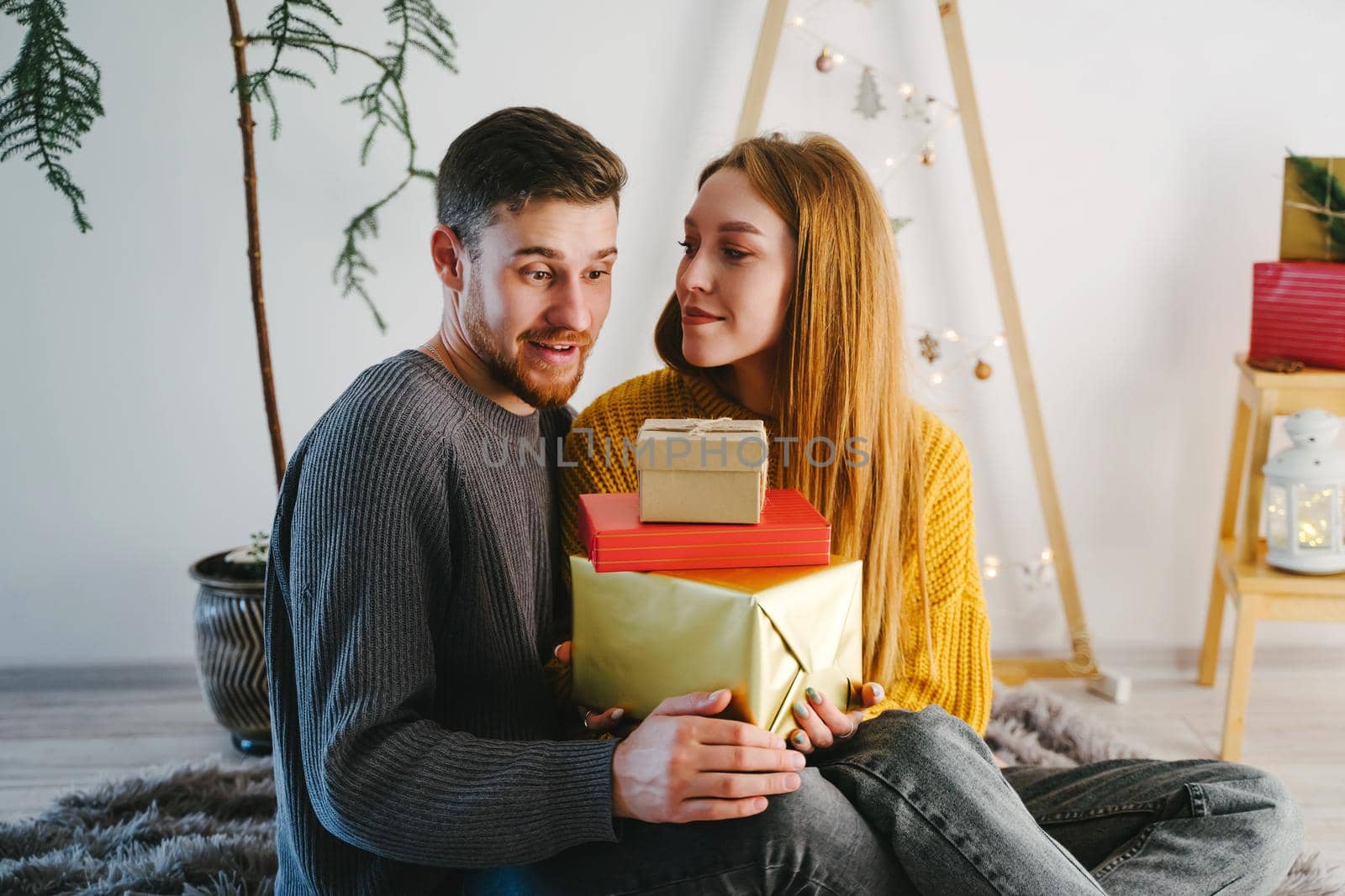 The boyfriend of the girl looks at the gifts in surprise. Couple in love is sitting in a Christmas location with a eco-friendly holiday decor.