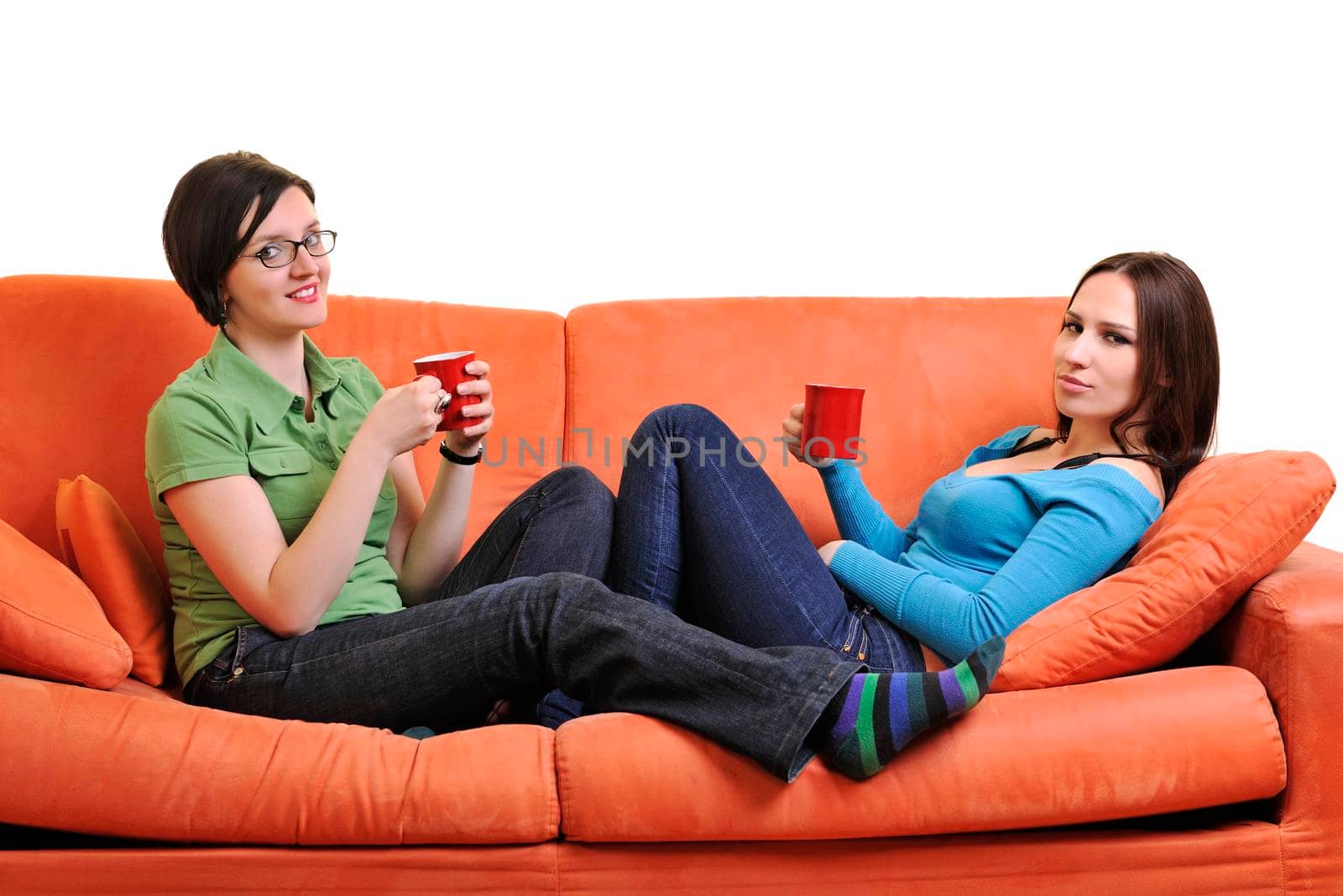 two young woman isolated on white with cup off coffee talking and chating isolated on whtie on orange sofa