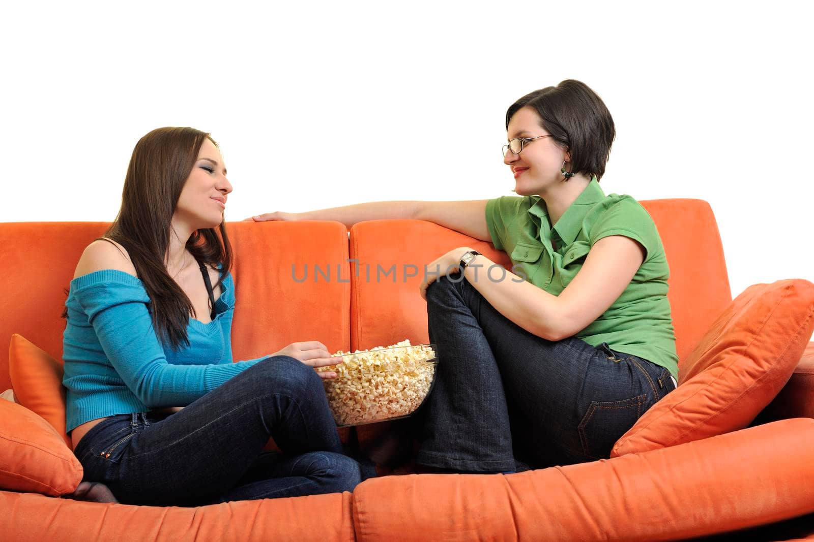 female friends eating popcorn and watching tv at home on orange sofa isolated on white