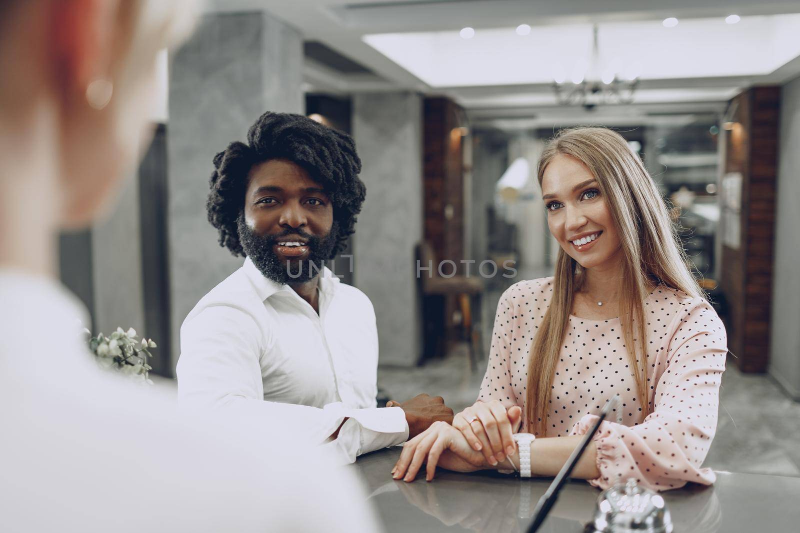 Business trip concept. Black man and caucasian woman businesspeople colleagues checking-in in hotel reception desk