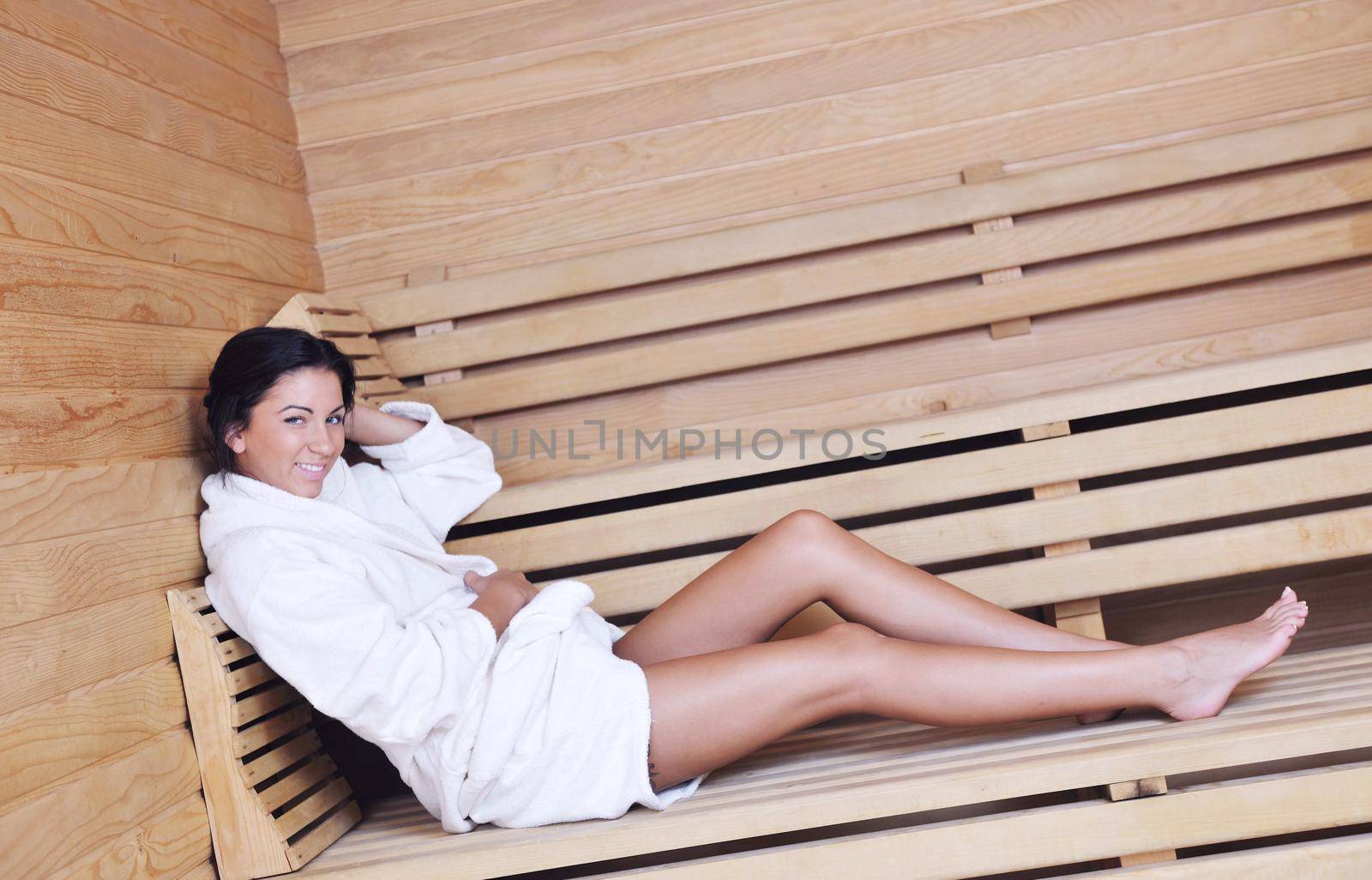 Pretty Young woman take a steam bath treatment at finish wooden sauna while wearing white towel