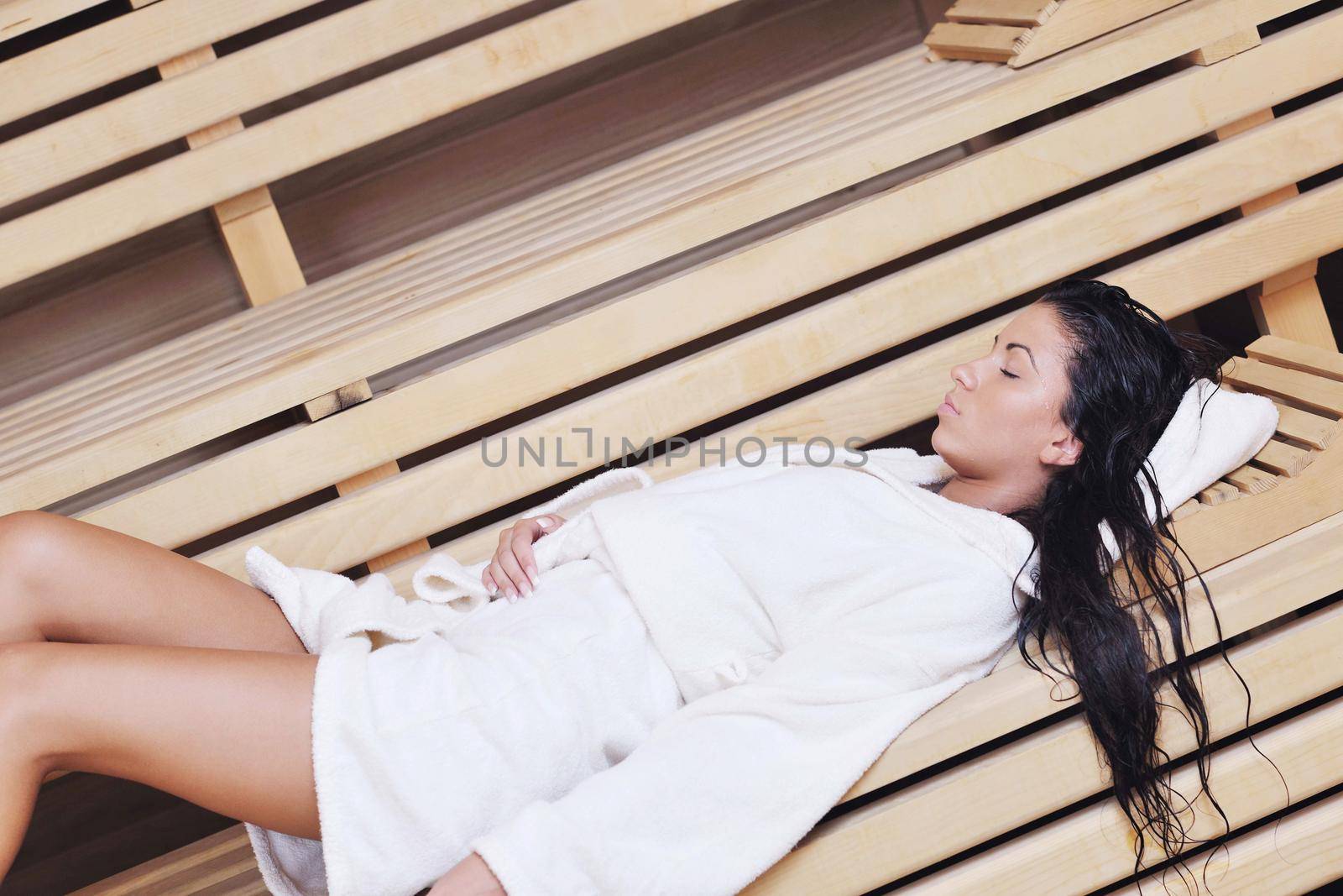 Pretty Young woman take a steam bath treatment at finish wooden sauna while wearing white towel