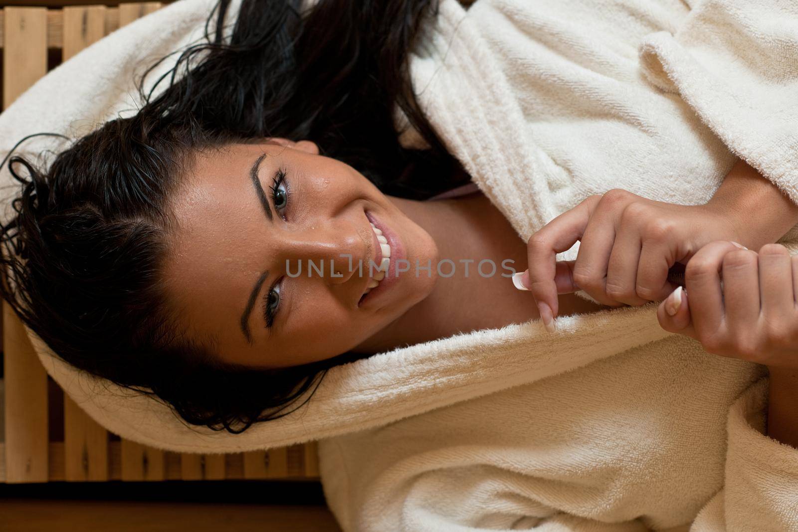 Pretty Young woman take a steam bath treatment at finish wooden sauna while wearing white towel