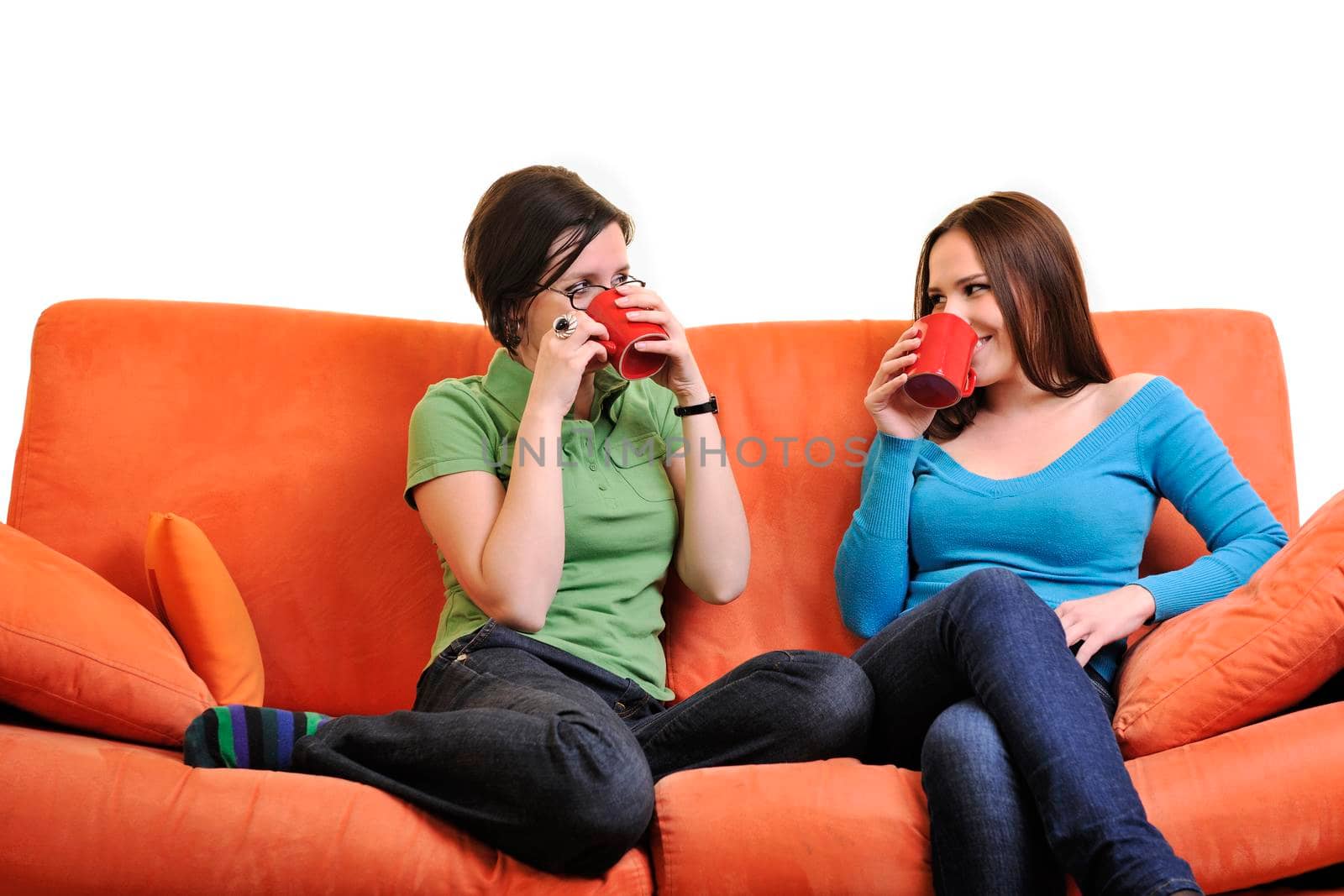 two young woman isolated on white with cup off coffee talking and chating isolated on whtie on orange sofa