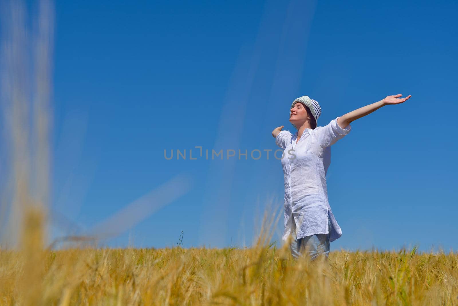 Young woman standing jumping and running  on a wheat field with blue sky the background at summer day representing healthy life and agriculture concept