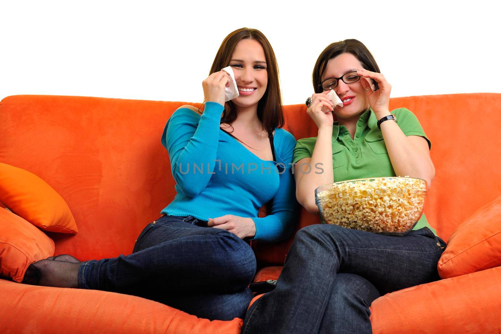 female friends eating popcorn and watching tv at home on orange sofa isolated on white